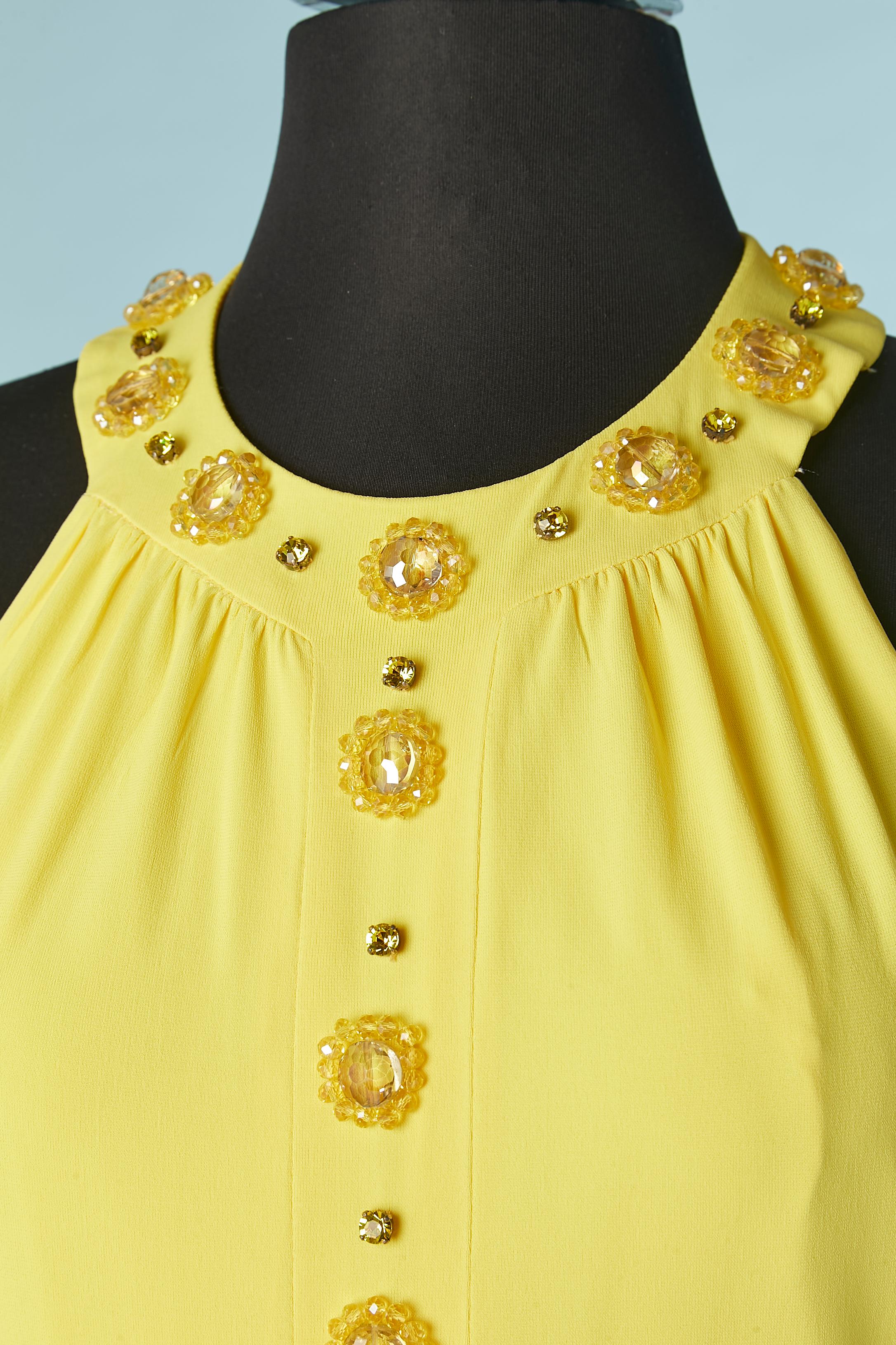 Vestido amarillo de jersey sin espalda con abalorios y adornos de strass. Composición del tejido: 76% acetato, 19% poliamida, 5% elastán . Cierre con botones de nácar en la parte superior central de la espalda;.División en la parte central