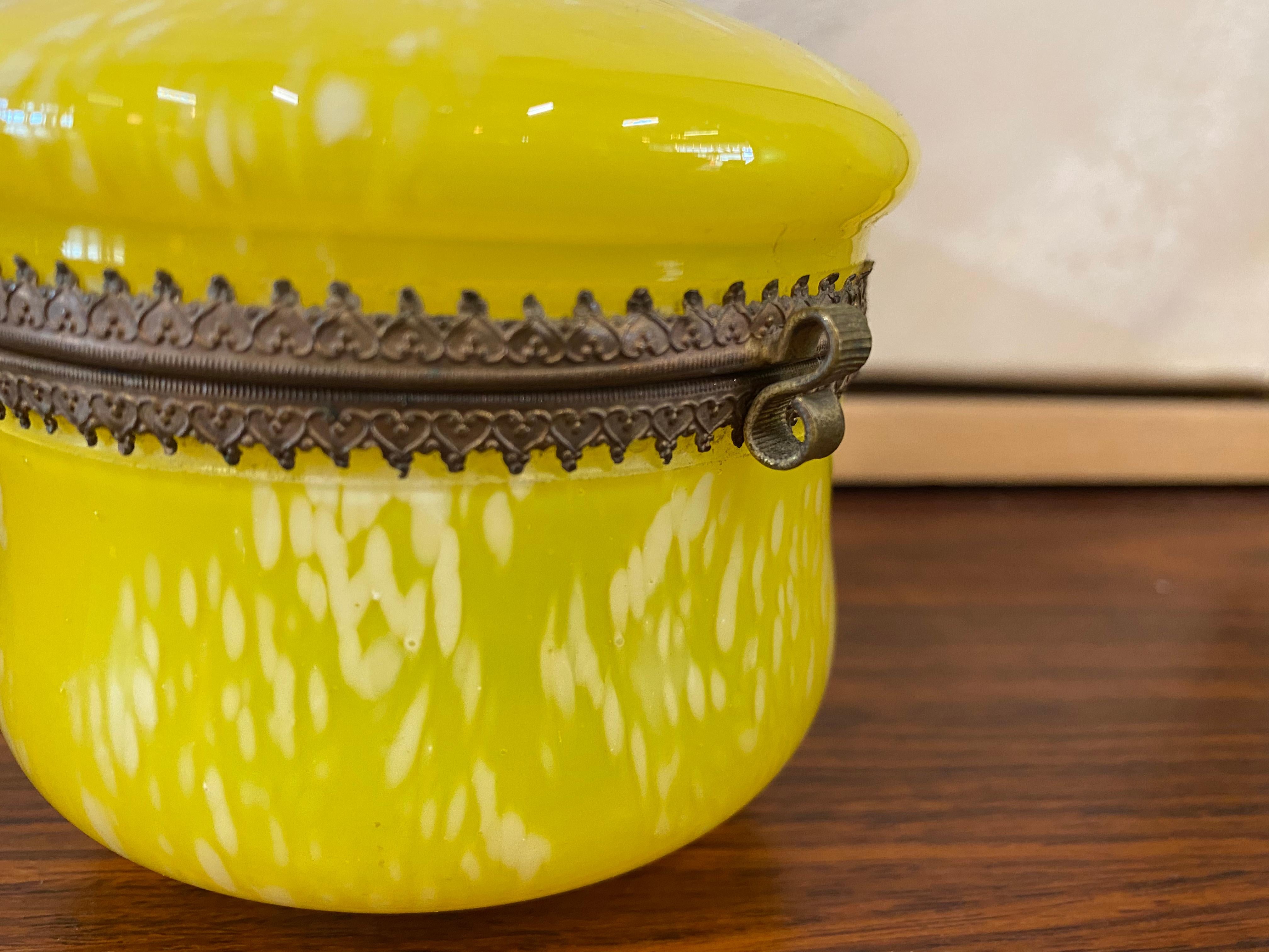 Biedermeier glass jar with lid from around 1900. An antique decorative accessory made of yellow colored glass and brass. The yellow glass is speckled white and mouth blown. The jar and lid each have a decorative brass rim and are connected by this.