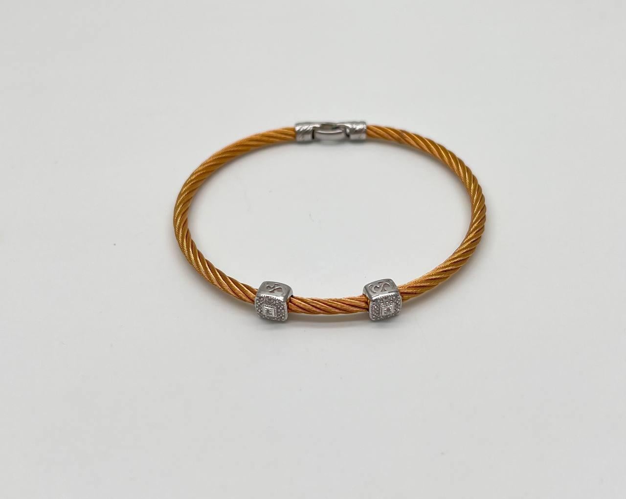 Crafted with a twisted cable design in a warm golden hue. Accented with two 18K White Gold cube charms, each adorned with intricate detailing and 0.10 CTW Diamonds. Secured with a sleek clasp.