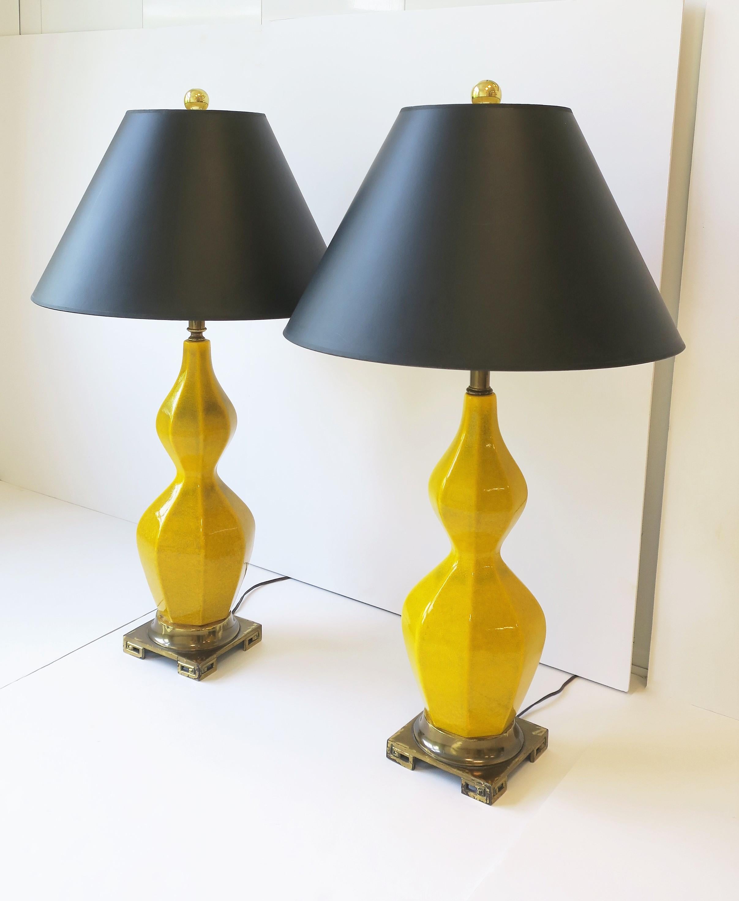 A pair of yellow ceramic table lamps with brass bases, Midcentury Modern period, circa mid-20th century, 1960s. Lamps have an hourglass and octagonal shape with a bras Greek-key like design base. In fine working order. 

Dimensions:
26.5