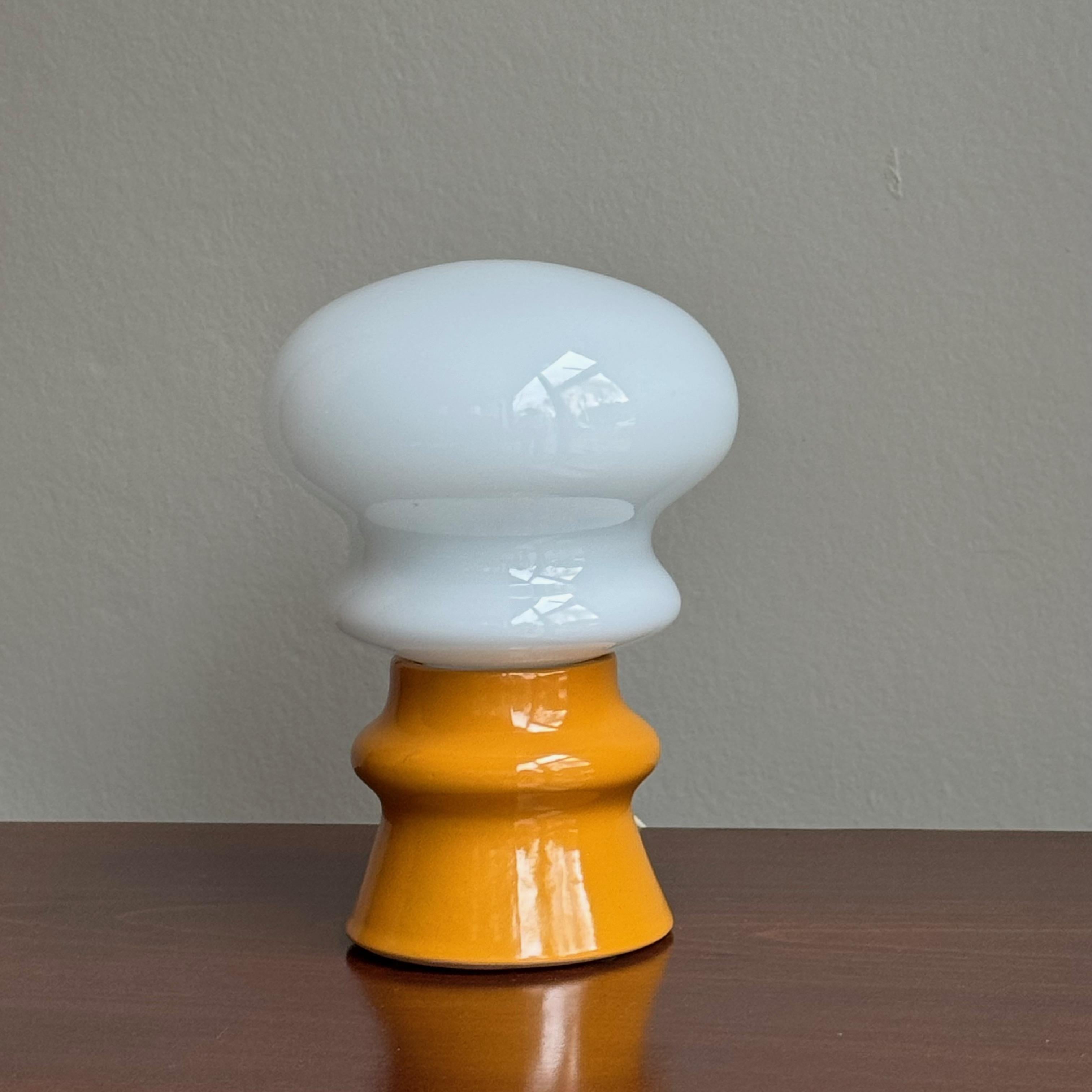 A petite, sculptural table lamp with a terracotta base, glazed in a vivid mustard-yellow, with an opaque, milk-glass shade. 

This table lamp was manufactured by Osvětlovací Sklo during the 1960s and was designed by Czech designer, Ivan Jakeš. This