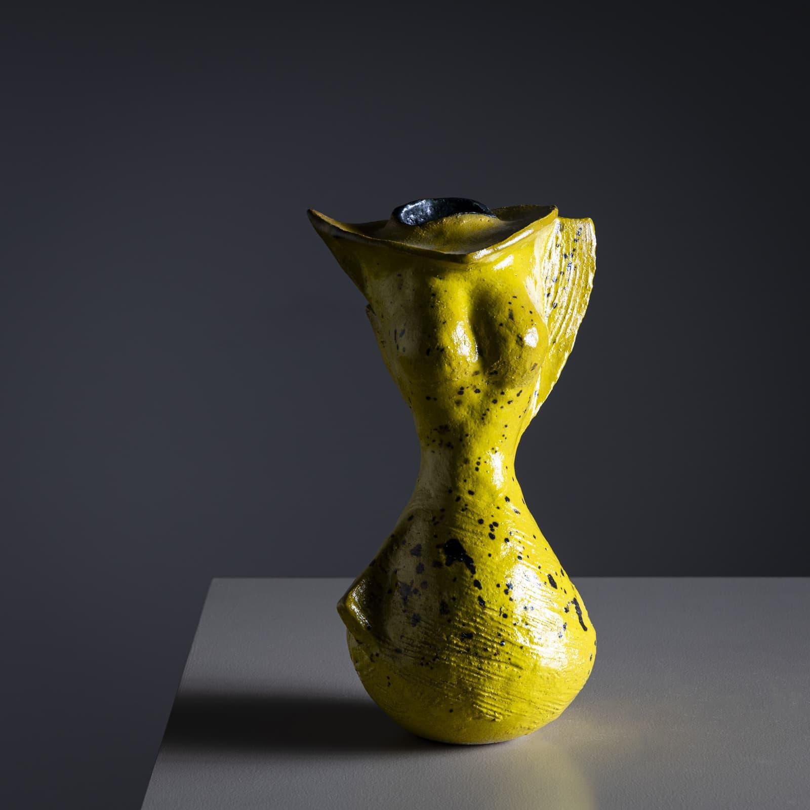 Vase en céramique émaillée jaune ayant la forme abstraite d'un torse féminin. La surface est mouchetée de points noirs. Le vase est signé POEMU sur le fond.

Poemu est un artiste français pluridisciplinaire connu pour sa créativité dynamique qui