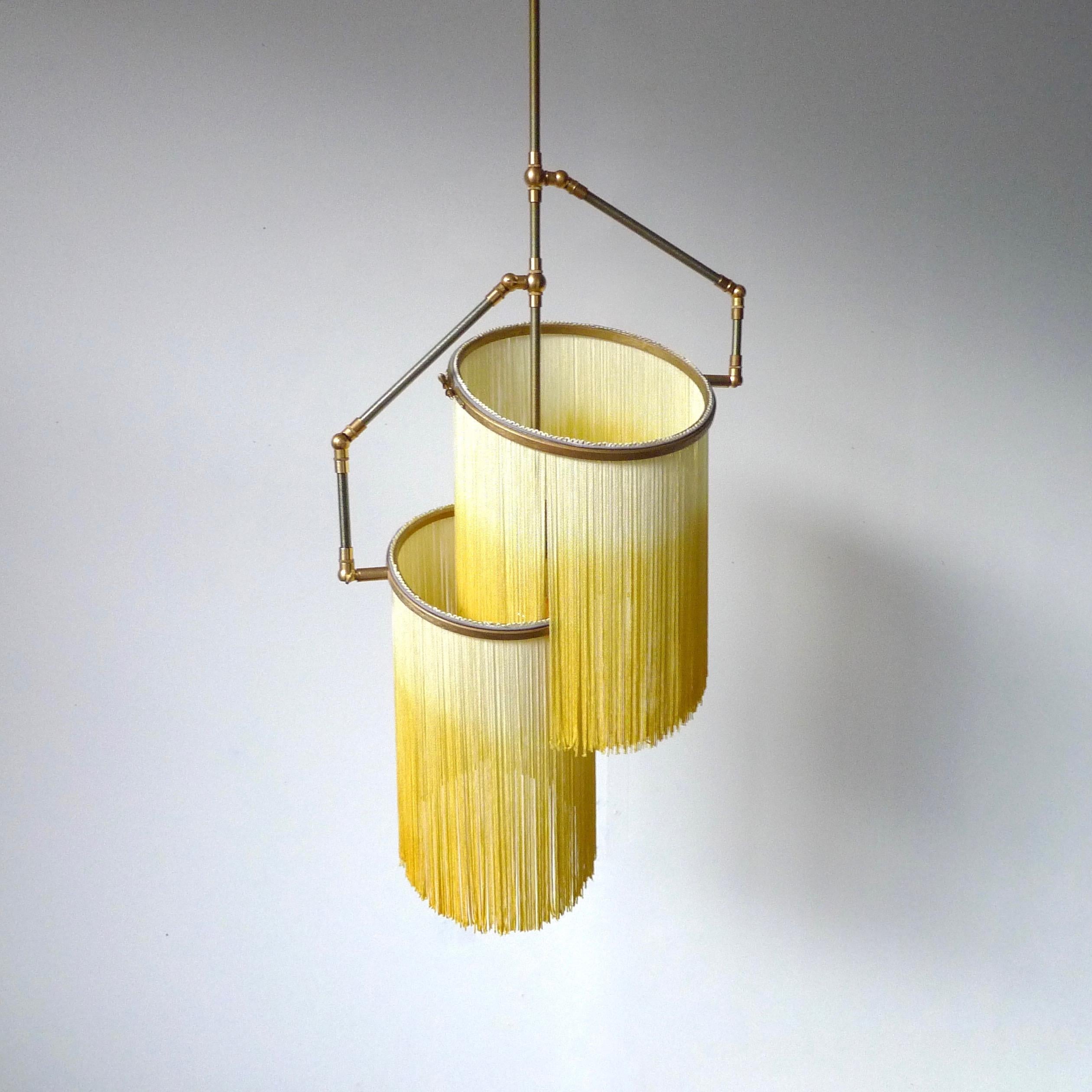 Yellow Charme Pendant Lamp, Sander Bottinga.

Dimensions: H 65 (can be customized) x W 38 x D 25 cm.
Hand-sculpted in brass, leather, wood and dip dyed colored Fringes in viscose.
The movable arms makes it possible to move the circles with