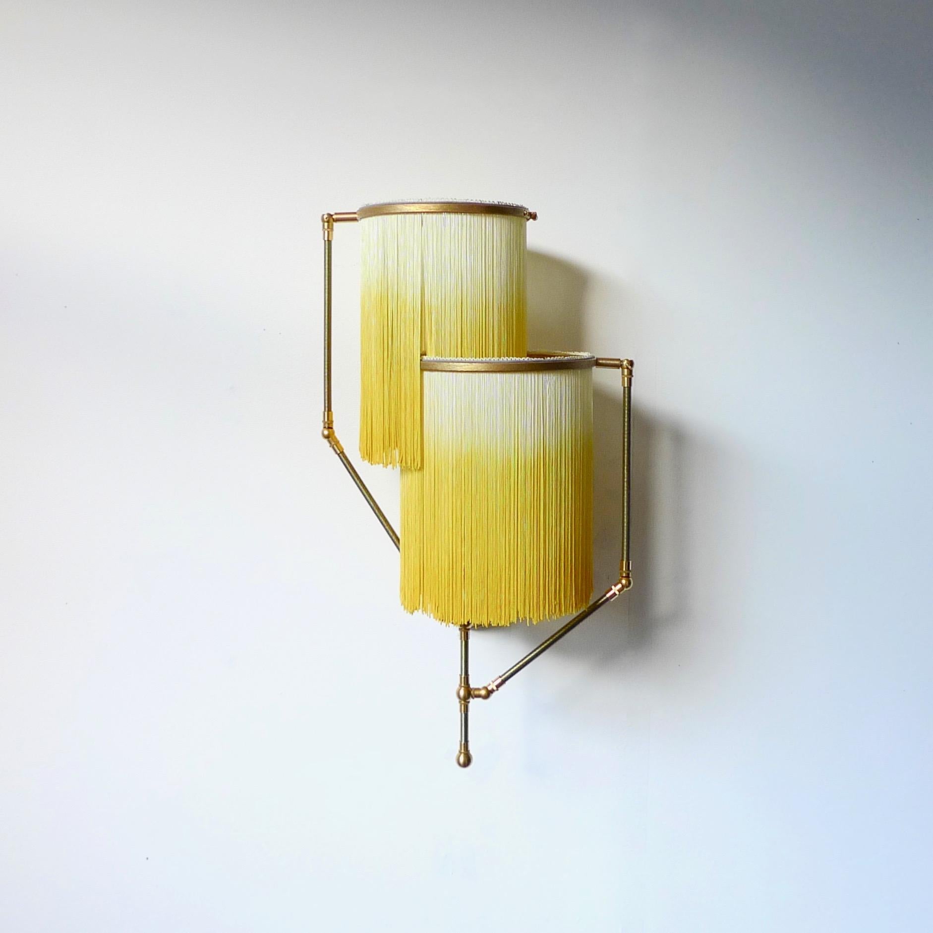 Yellow Charme sconce lamp, Sander Bottinga

Dimensions: 50 x W 38 x D 27 cm
Handmade in brass, leather, wood and dip dyed colored Fringes in viscose.
The movable arms makes it possible to move the circles with fringes in different positions.
So you