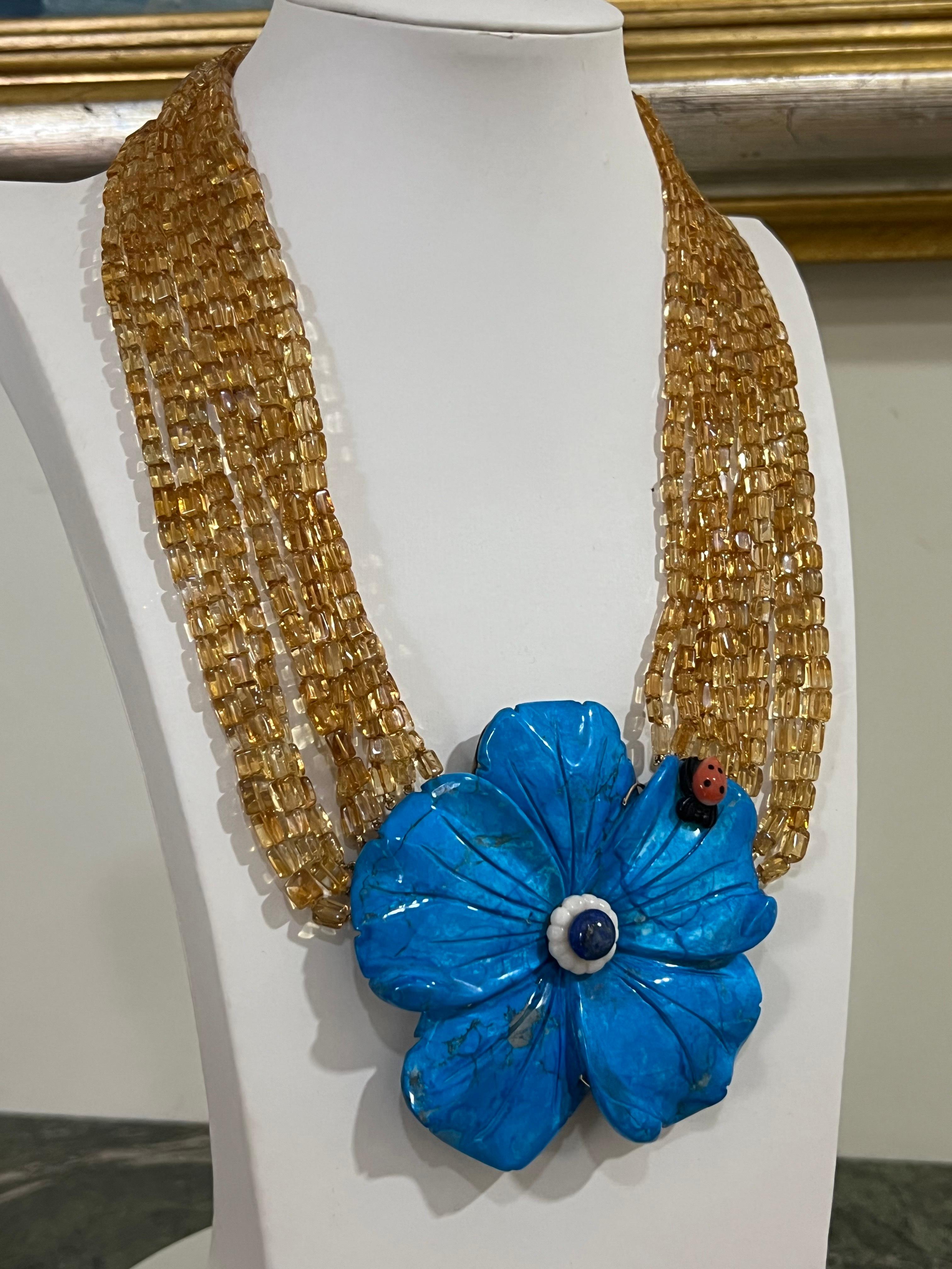 Wonderful multi-strand necklace made at the beginning of the 2000s composed of many strands of citrine barrels adorned with a magnificent blue flower as a central breastplate on which rests a small onyx ladybug, the structure behind the flower is