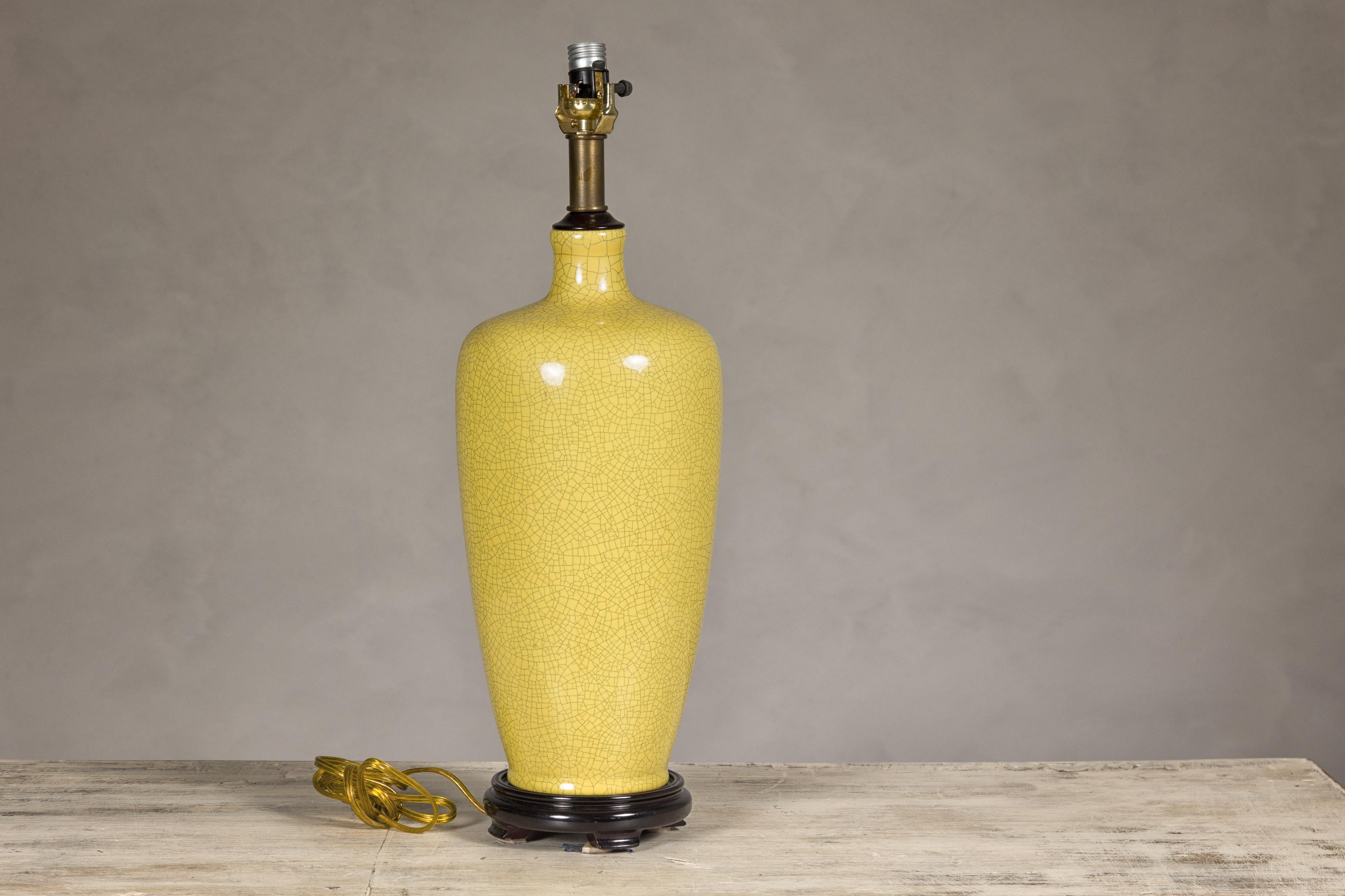 Un vase en céramique émaillée jaune craquelé transformé en lampe de table et monté sur une base circulaire en bois avec de petits pieds. Cette lampe de table, qui était à l'origine un vase en céramique émaillée jaune craquelé, a été judicieusement
