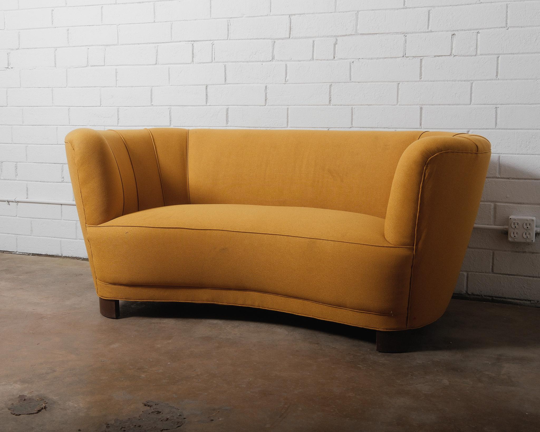 This Danish Curved Banana Sofa 1940s loveseat, designed in the style of Viggo Boesen, is a hallmark of mid-century Scandinavian design. This piece traces its origins to a period spanning from the late 1930s to the early 1950s, when such sofas were a