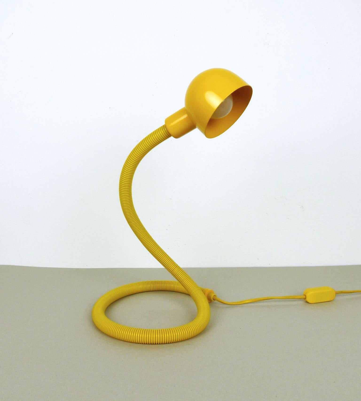 This yellow table lamp from the 1970s features a long, flexible swan neck and a rotating metal lampshade. Its long, slim body is shaped like a snake and can be bent into different positions. The lamp has an E 14 bulb socket and it is in very good