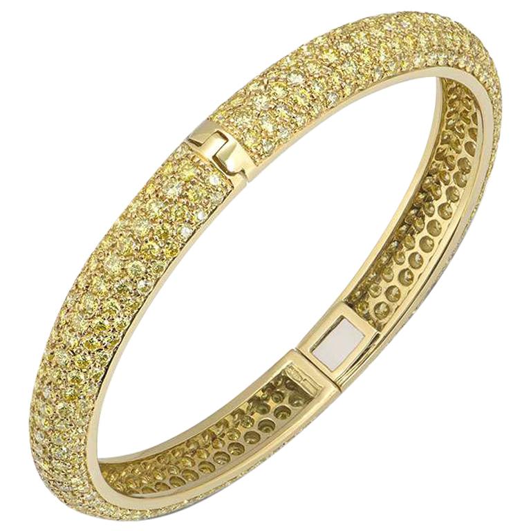 An 18k yellow gold diamond set hinged bangle. The bangle is pave set with round brilliant cut yellow diamonds, varying in intensity. The diamonds have a total approximate weight of 5.60ct. The bangle measures 7mm in width and would fit a wrist size