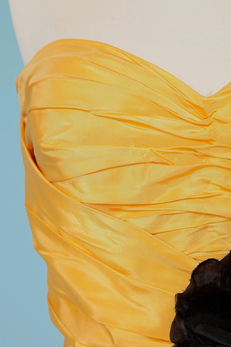 Gelbes drapiertes Bustierkleid aus Seidentaft mit Schleife und schwarzer Blume. Reißverschluss und Haken und Ösen in der hinteren Mitte. Bügel-BH ( 90 cm) Seitlich entbeint. Drapierter Schulterschal (Länge 100cm) mit Blume zum Aufstecken. Auch die