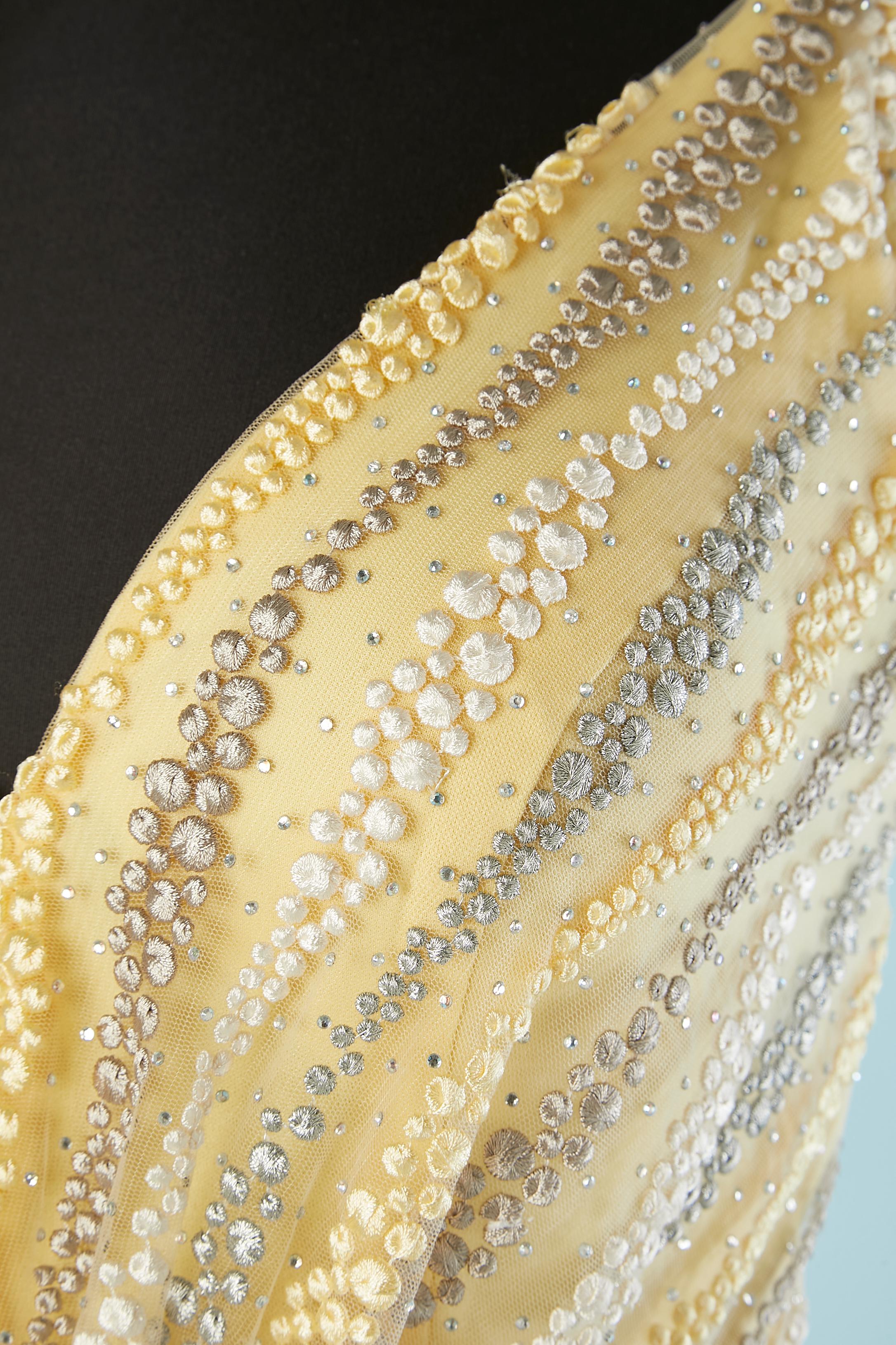 Abito da sera giallo con ricami in filo e strass su una base di tulle.
Nastro in gros-grain beige sulla tracolla e in vita. Gancio e occhio nella parte centrale della schiena. 
Reggiseno imbottito. Fodera fino a metà giro. Fiocco al centro della