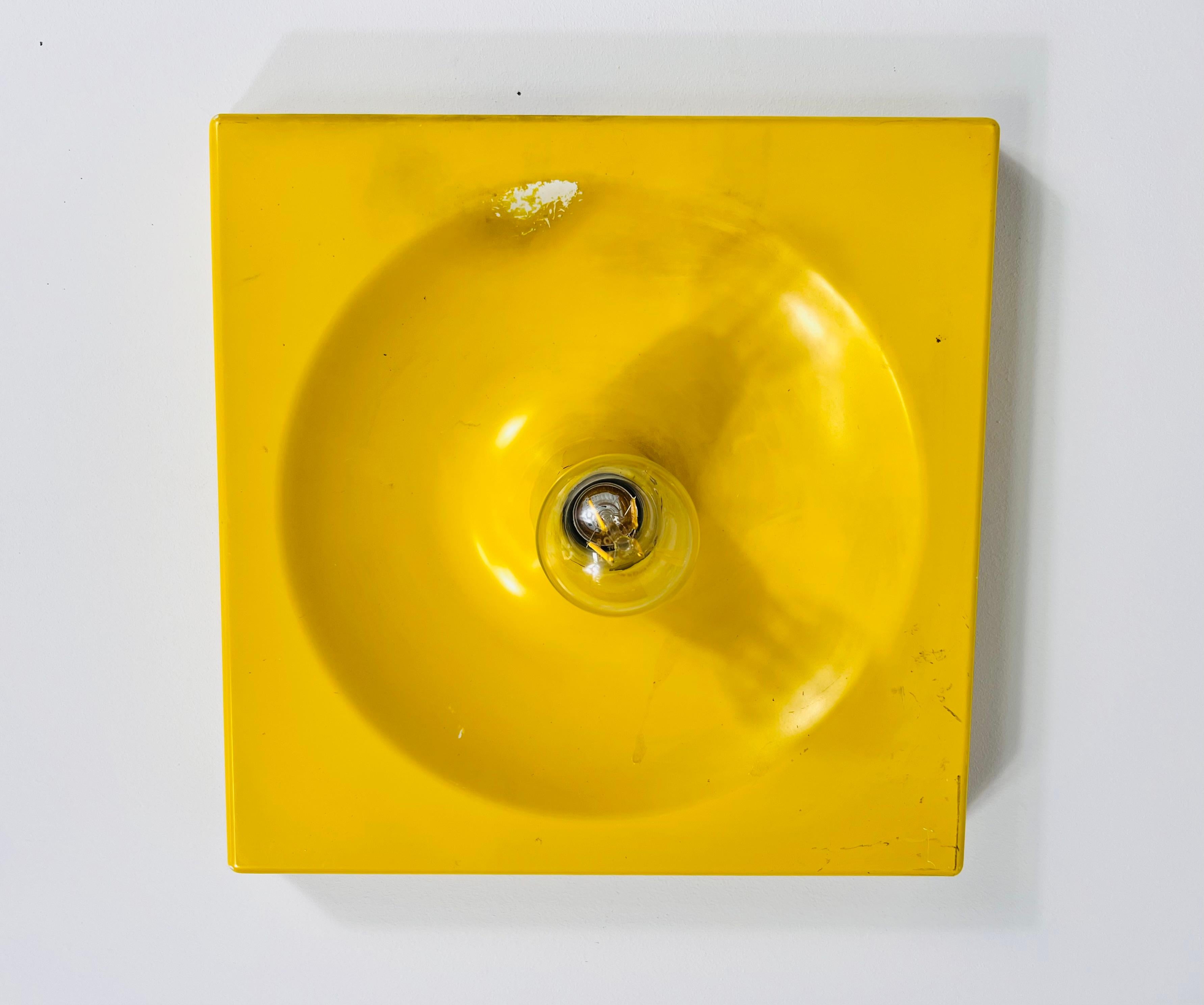 This Space Age flush mount or wall lamp, crafted by Kaiser in Germany during the 1970s, embodies the innovative design ethos of the era. Designed by Klaus Hempel, the lamp features a sleek, full metal body with a beautiful yellow finish that