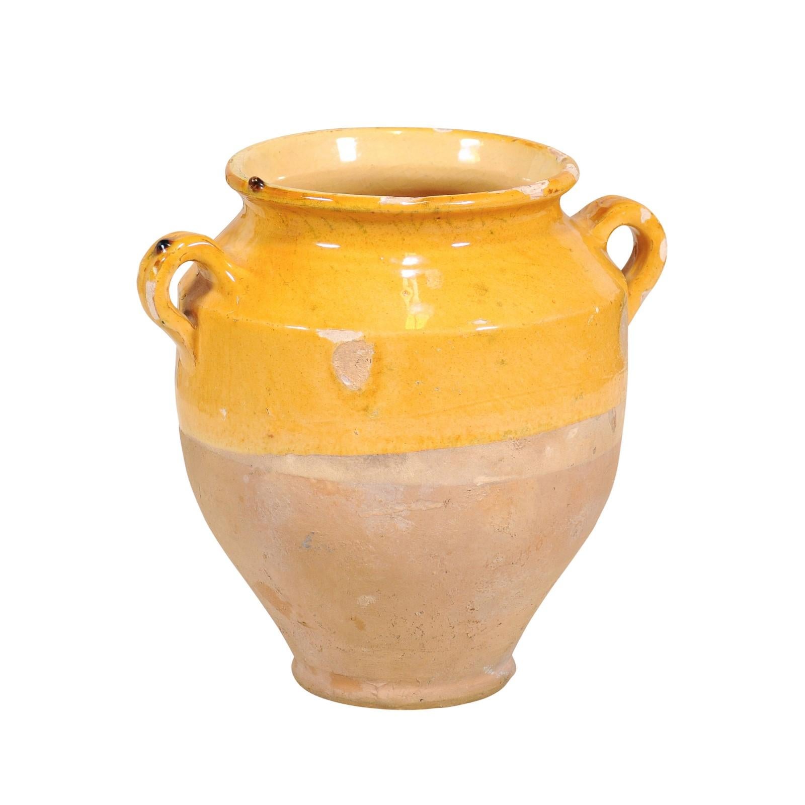 A French Provincial pot à confit pottery from the 20th century with yellow glaze, two lateral handles and rustic character. Step into the rustic charm of the French countryside with this 20th-century French Provincial pot à confit, a piece that