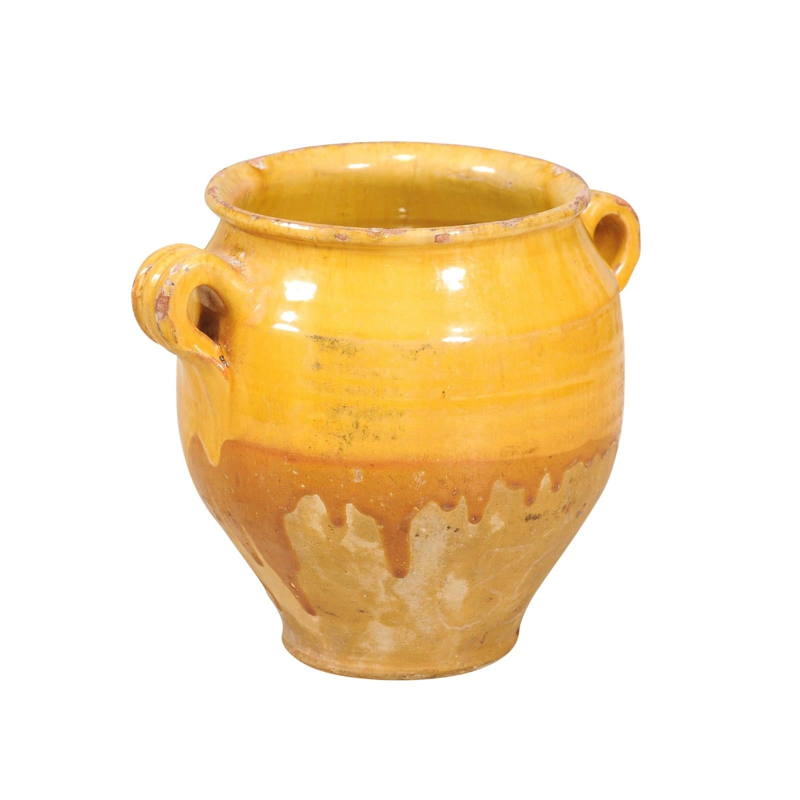 A French Provincial double handled pot à confit from the 20th century with yellow glaze and nice rustic character. This French Provincial pot à confit, with its inviting yellow glaze, is a delightful representation of 20th-century rustic charm. The