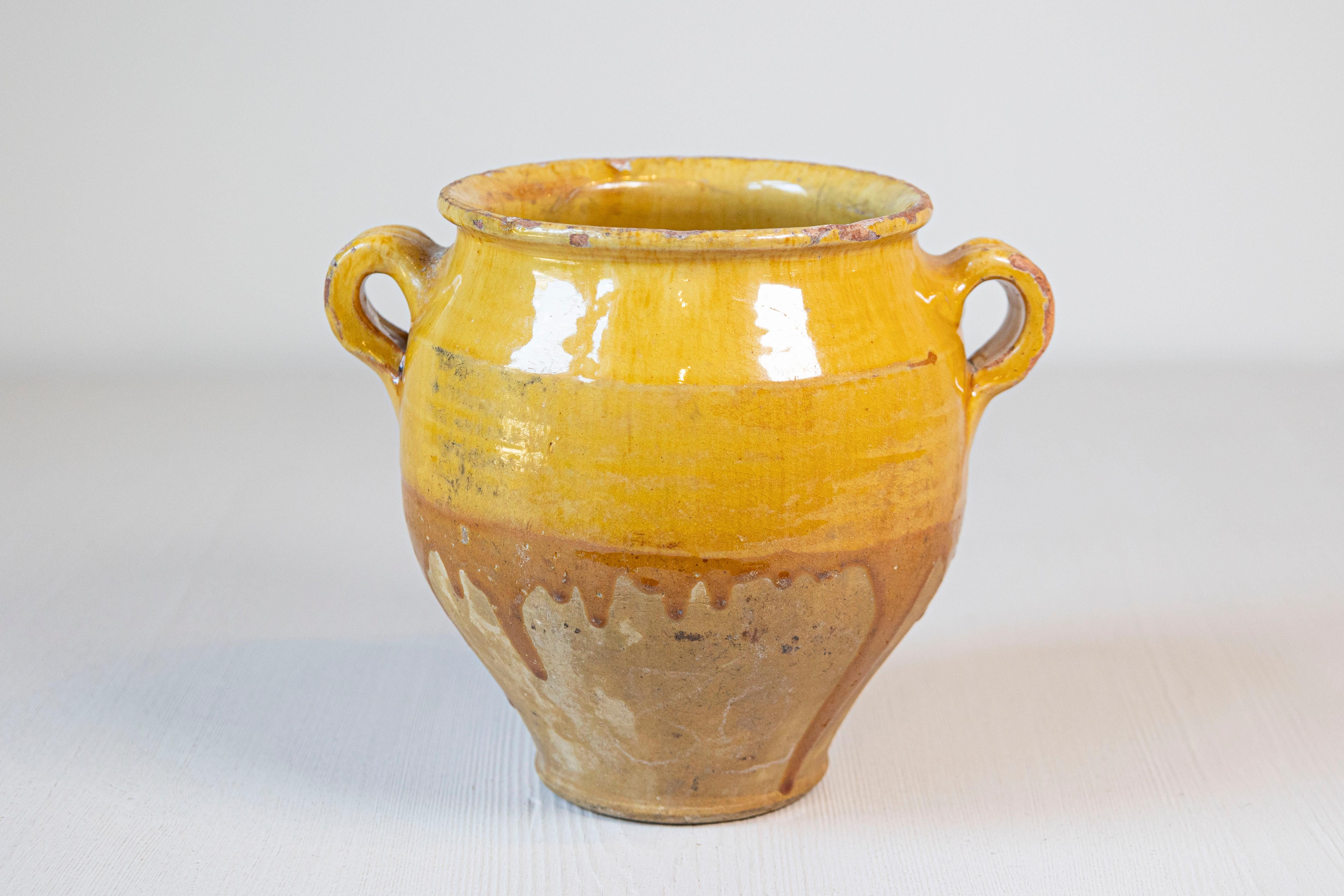 A French Provincial double handled pot à confit from the 20th century with yellow glaze and nice rustic character. This French Provincial pot à confit, with its inviting yellow glaze, is a delightful representation of 20th-century rustic charm. The