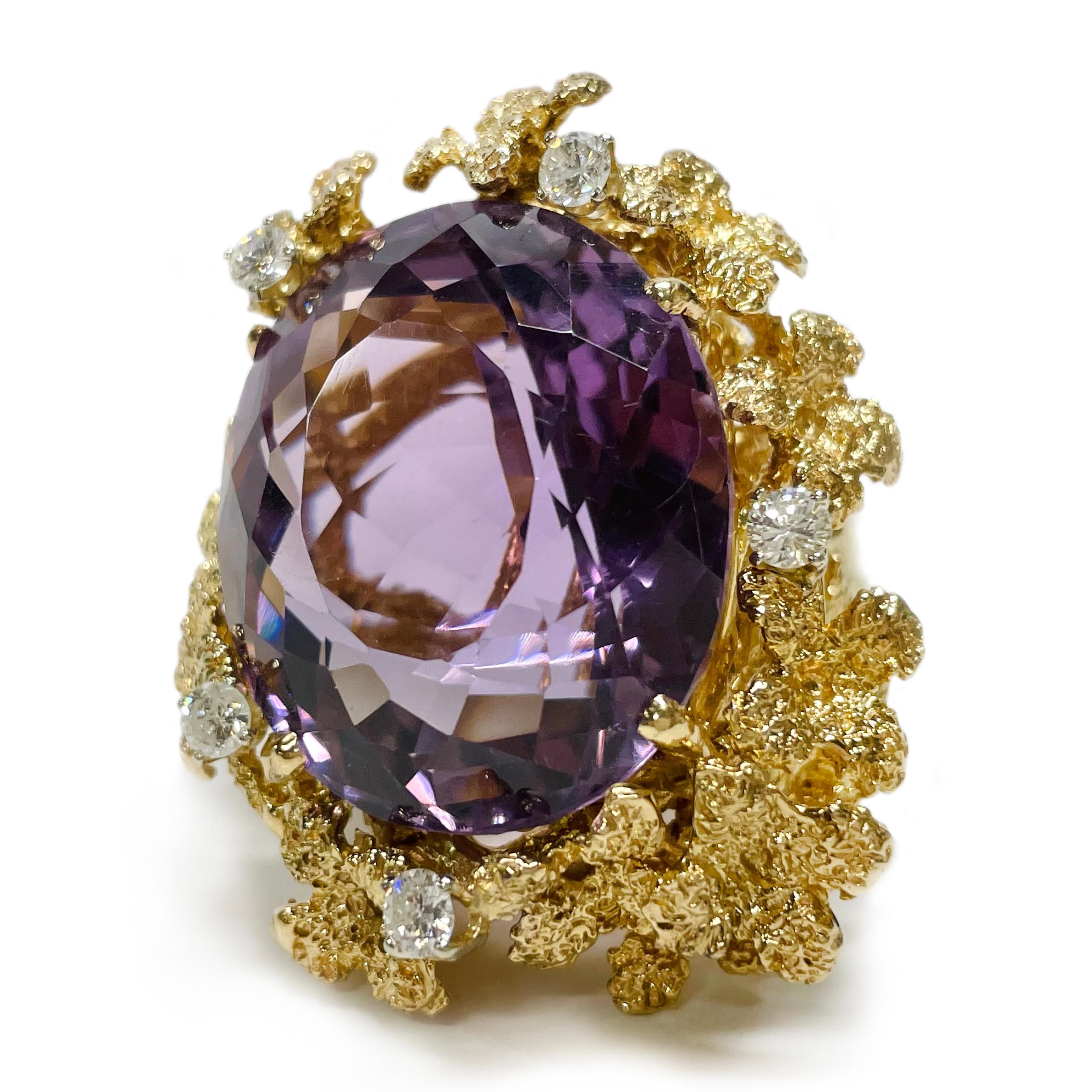 18 Karat Yellow Gold Amethyst Diamond Cocktail Ring. The ring features a large 27.7 x 23.3mm oval-cut Amethyst, five round 3.4mm prong-set diamonds and multiple textured gold flowers. The diamonds have a total carat weight of 0.75ctw. This is a true