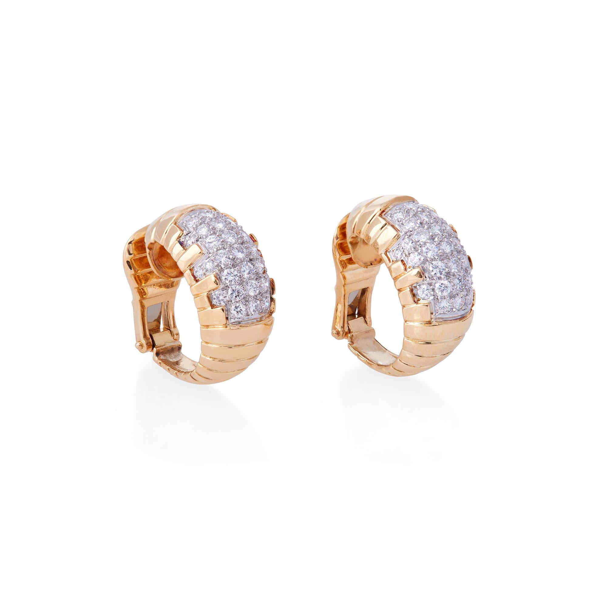 A charming pair of huggie hoop earrings crafted in 18 karat yellow gold.  The high polished gold features a ribbed design with approximately 1.6 carats of round cut diamonds set in a cutout design at the center of each earring.  The earrings measure