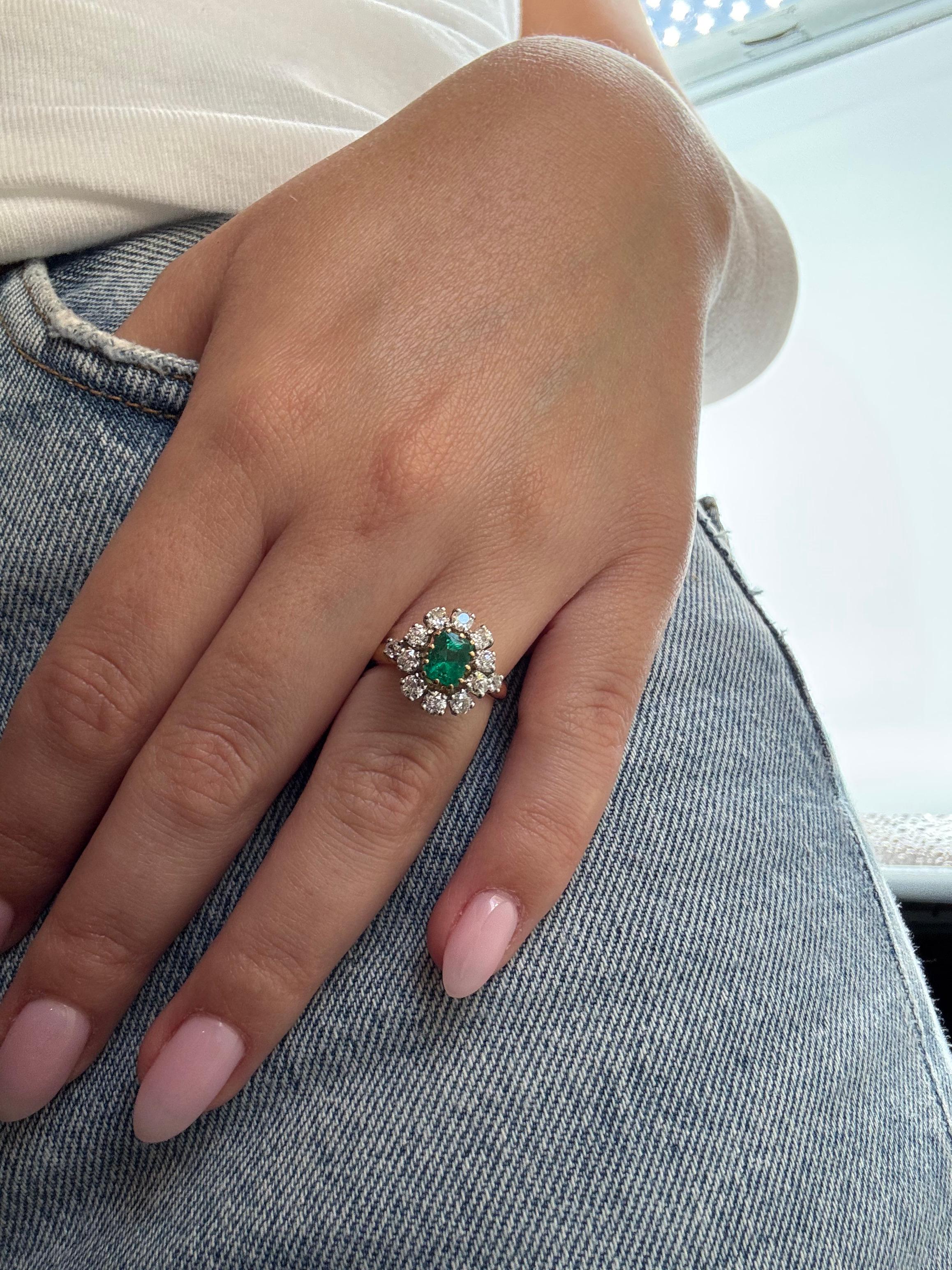 Une charmante bague de style marguerite réalisée en or jaune 18K et platine (950‰), centrée sur une vibrante émeraude taille coussin d'environ 1,10 carats. L'émeraude est encadrée d'un seul halo de dix diamants taille brillant totalisant environ