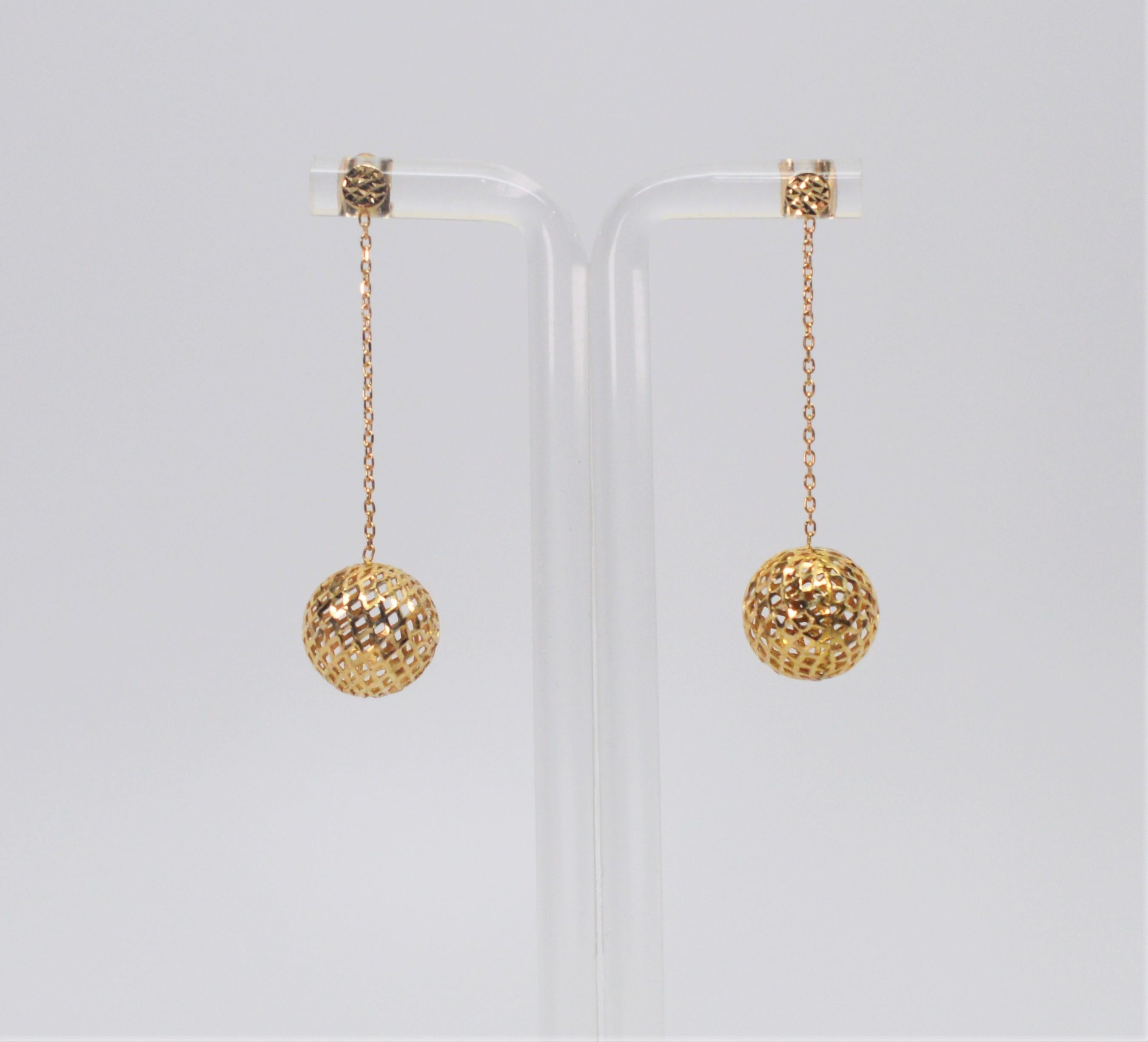 Flirty and fresh, bright fourteen carat yellow gold open weave balls catch the light and glisten while being suspended from 1-1/4 inch fine gold chain secured by post earring closures with hammered metal details.