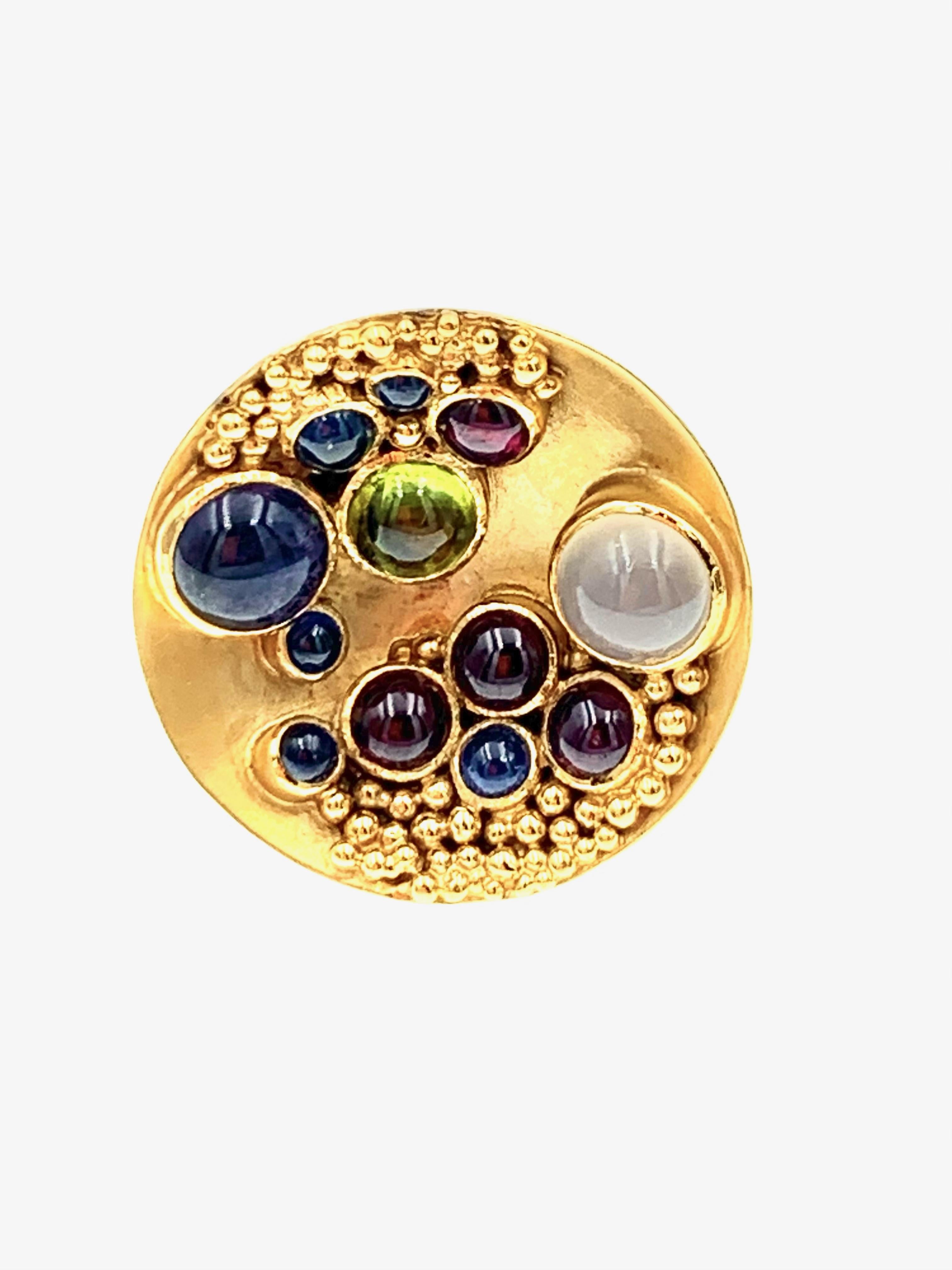 Hand made in 18 karat yellow gold with one Peridot cabochon, one Iolite cabochon, one Moonstone cabochon, 5 cabochon Blue Sapphires, 4 Rubelite cabachons and approximately 54 gold beads, in an inverted dome of brushed gold this ring is part of our