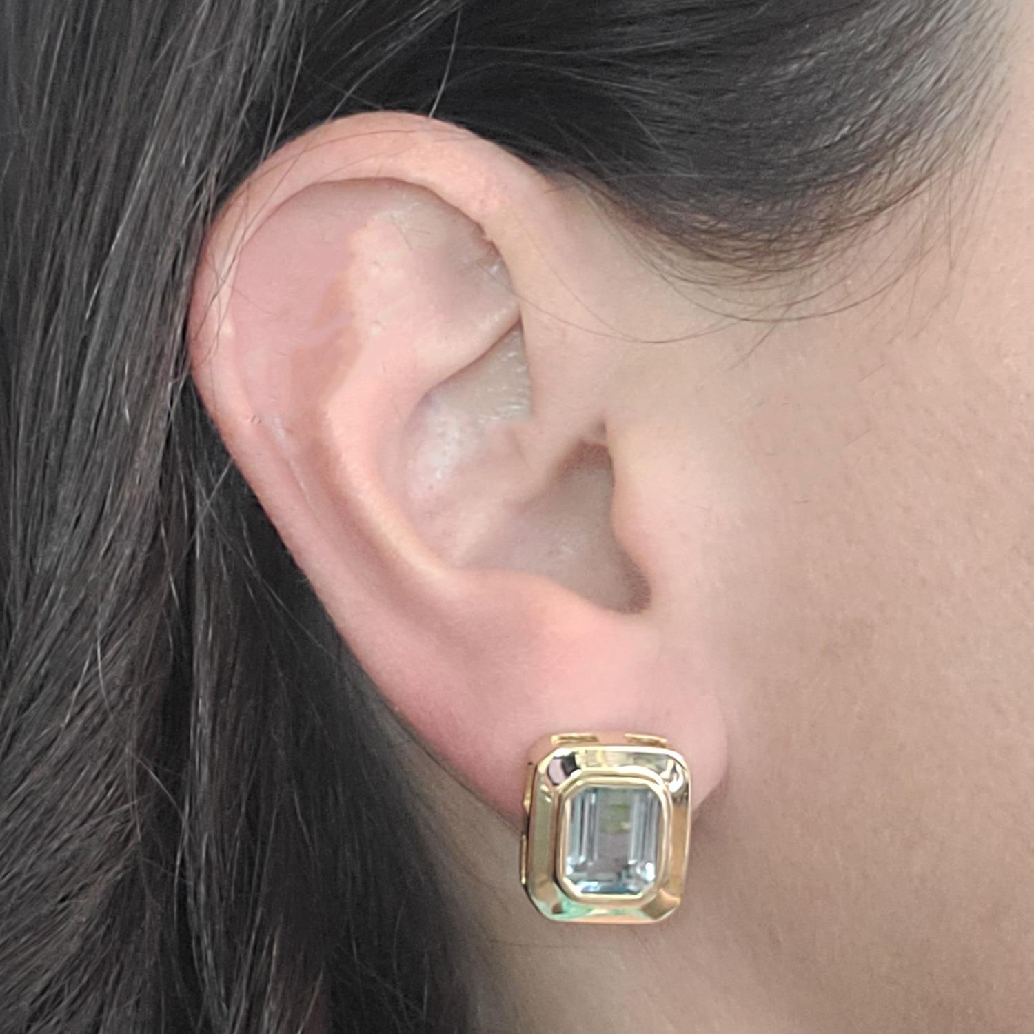 14 Karat Yellow Gold Earrings Featuring 2 Bezel Set Emerald Cut Blue Topaz Measuring 7.5mm x 10mm. Pierced Post with Omega Clip Back. Finished Weight Is 10.0 Grams.