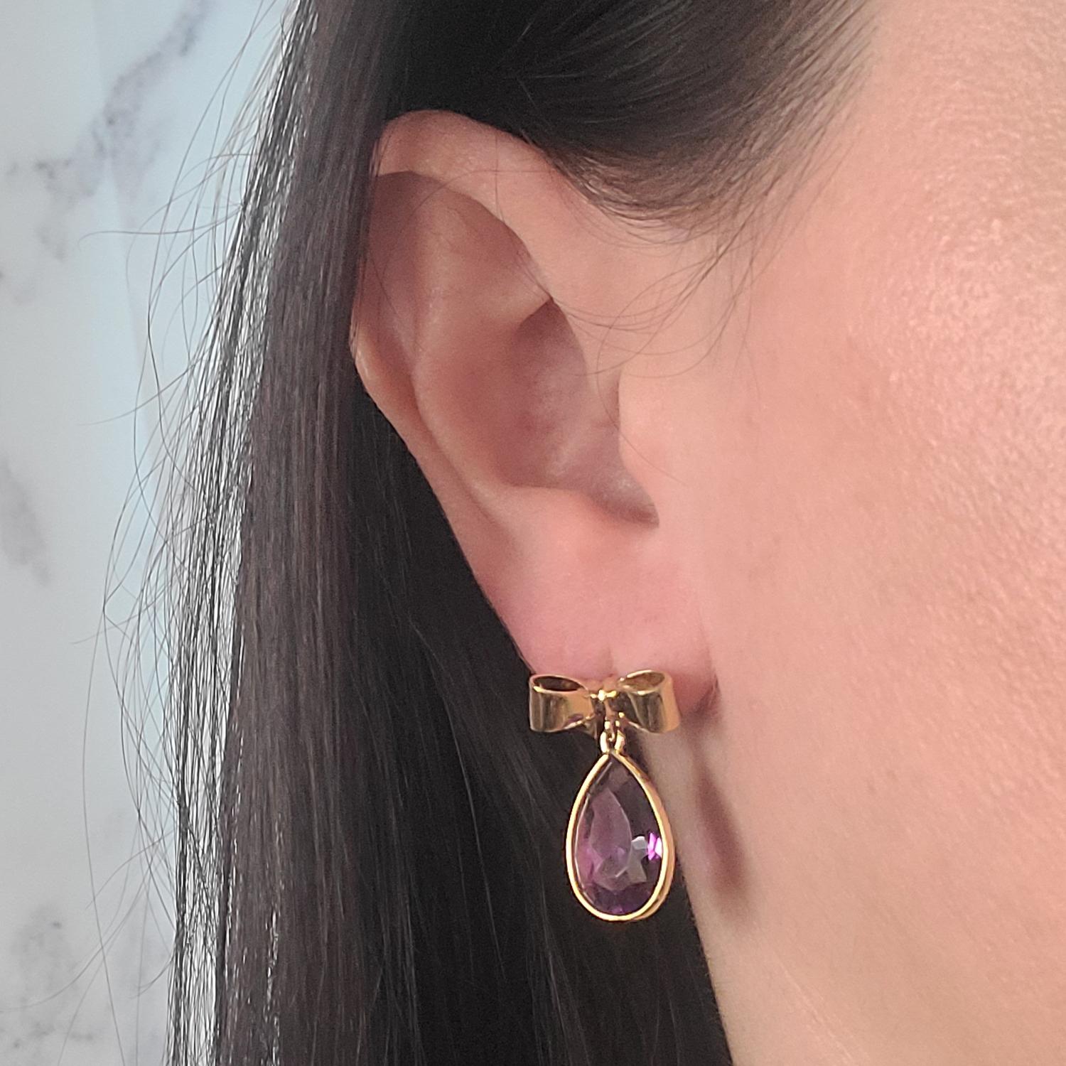 Well-made 18 Karat Yellow Gold Solid Bow Drop Earrings Featuring 2 Bezel Set Pear Cut Amethysts Totaling Approximately 10 Carats. 1 Inch Length. Pierced Post with Friction Back. Finished Weight Is 9.2 Grams.