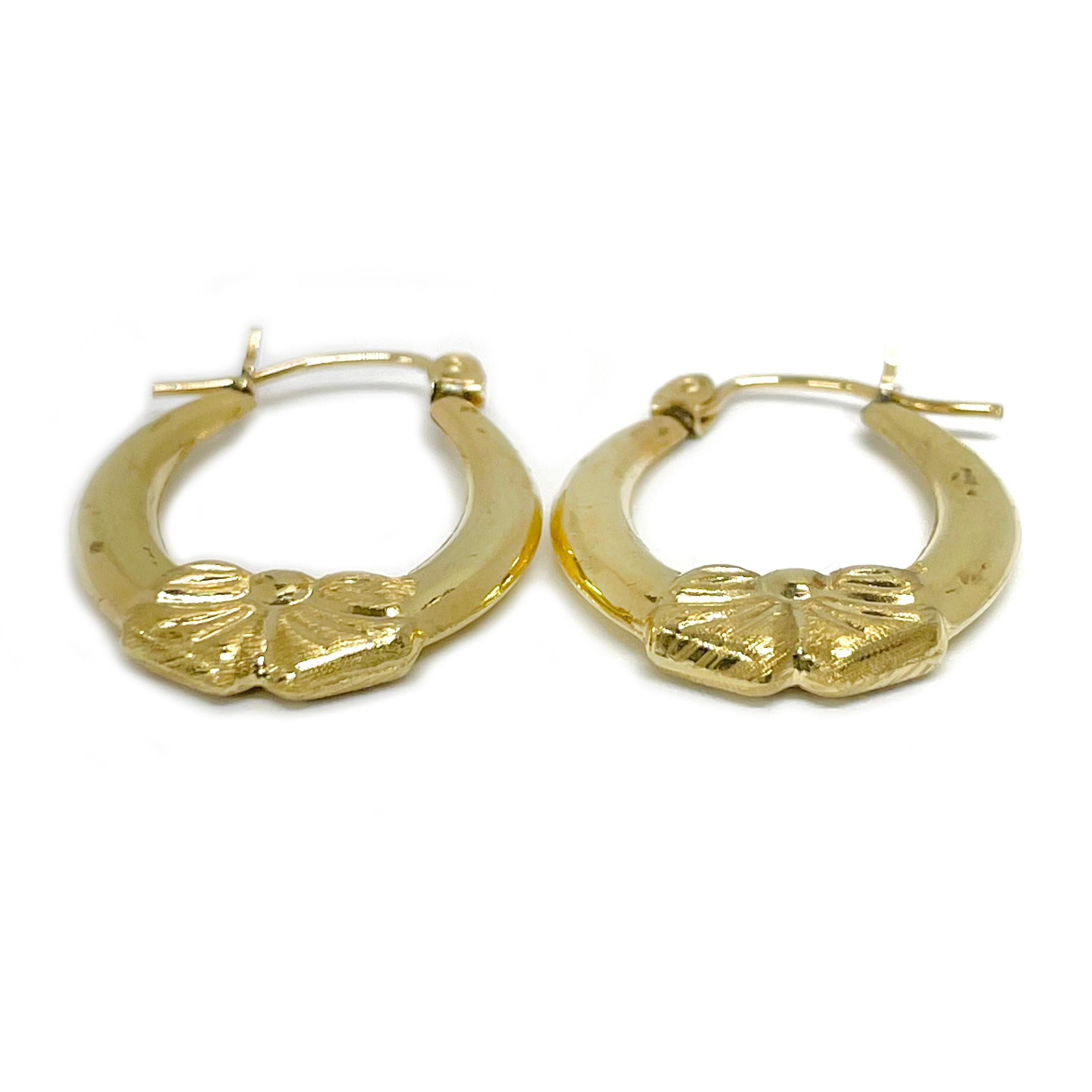 14 Karat Yellow Gold Bow Hoop Earrings. These lightweight hollow hoops feature a textured bow detail at the bottom of the hoop with an overall smooth shiny finish. The earrings measure 23mm high x 18.6mm wide. The earrings have a hoop wire closure