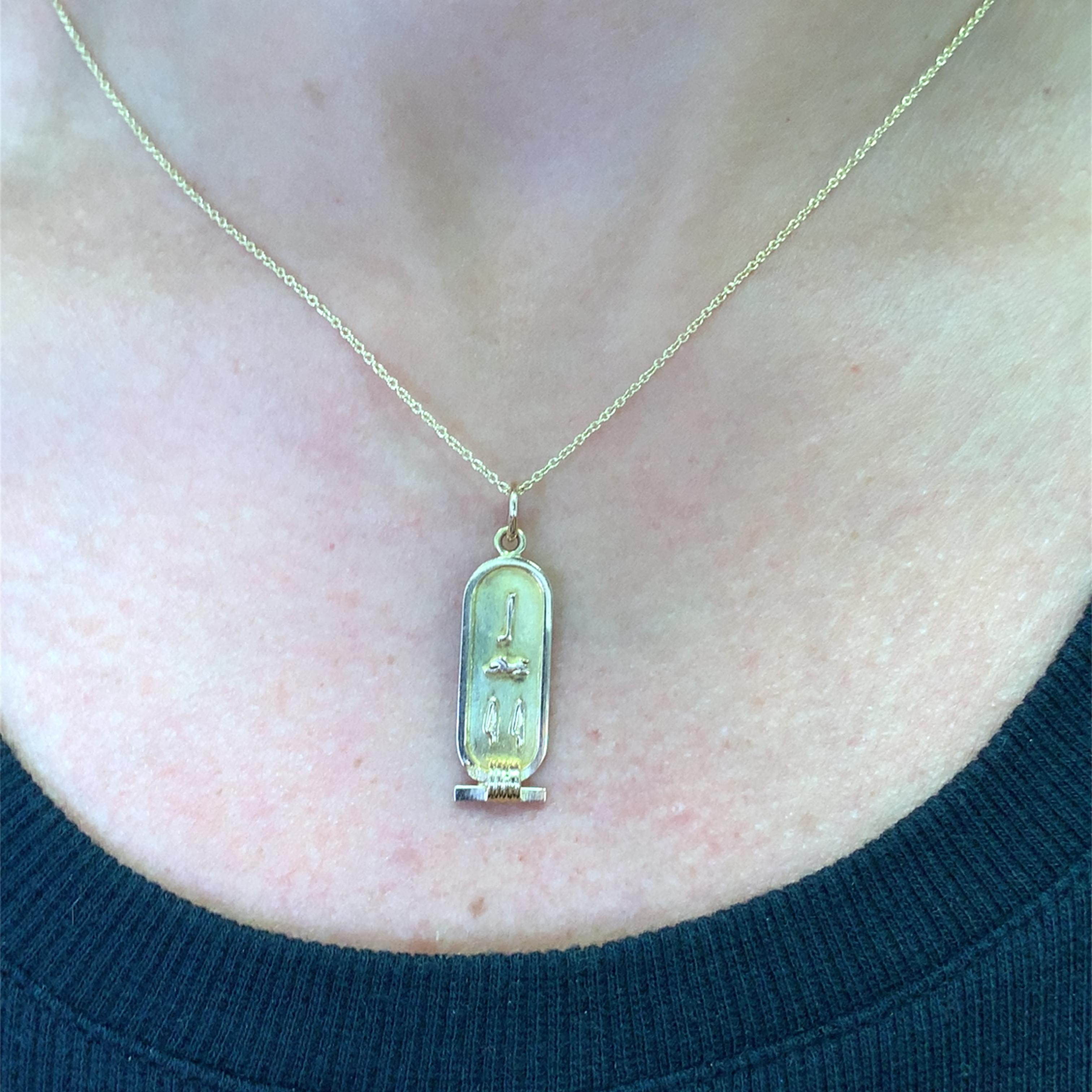 Embrace ancient mystique with this 18k new yellow gold cartouche pendant. The cartouche, a symbol of protection and nobility in ancient Egypt, features intricate hieroglyphic engravings. Suspended from a delicate yellow gold chain, this pendant adds