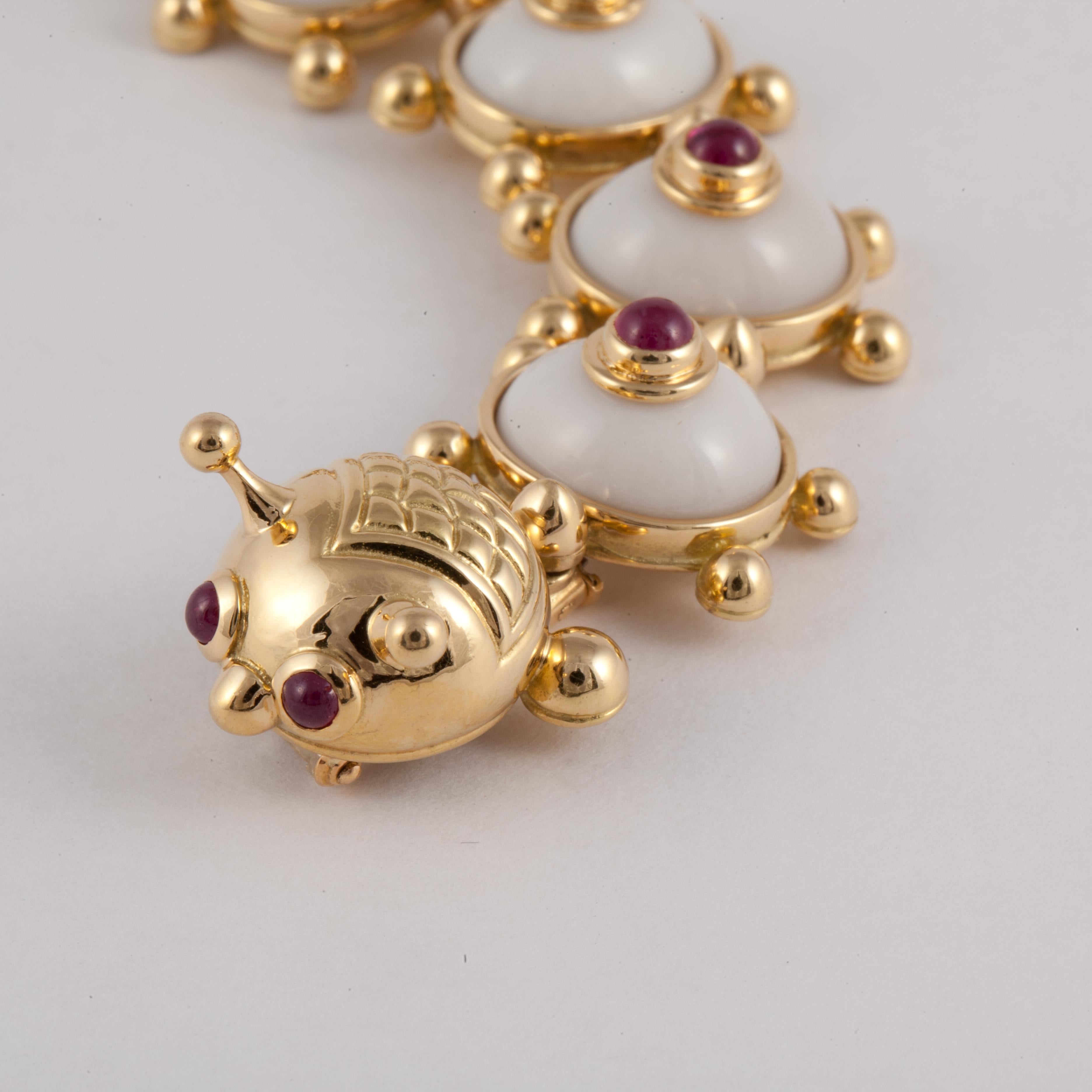 18K yellow gold ceramic and ruby novelty brooch, by Eva Legoura, French, circa 1990.  Designed as a stylized centipede, composed with a line of graduated articulated circular links set with domed ceramic panels with central cabochon ruby motif, each