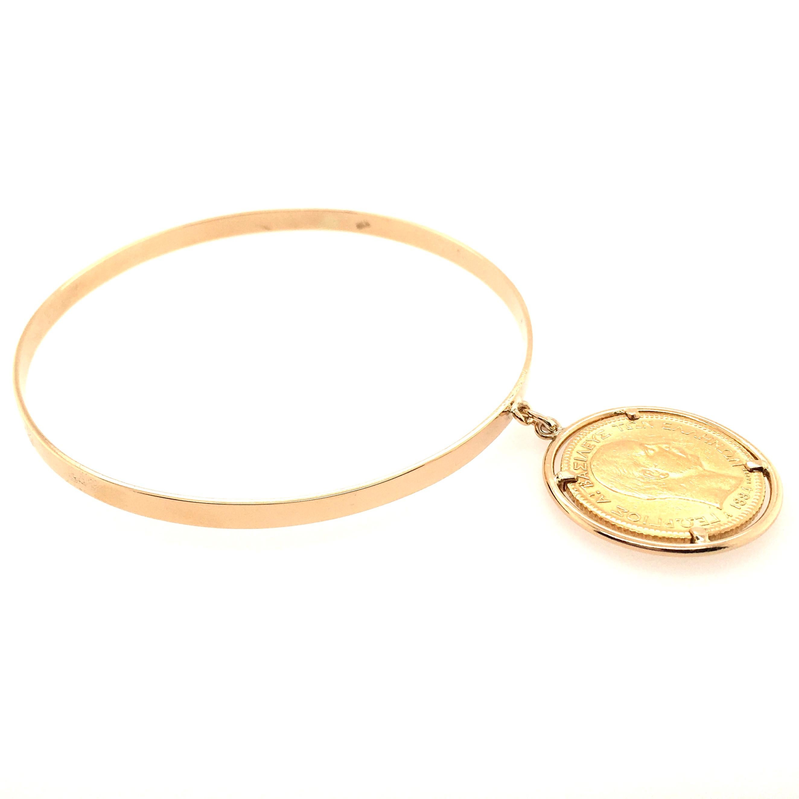 An 18 karat yellow gold bangle bracelet, with 22 karat yellow gold restrike 1884 50 Franc coin, within an 18 karat yellow gold frame. Diameter of coin is approximately 1 inch, gross weight is approximately 18.2 grams. 