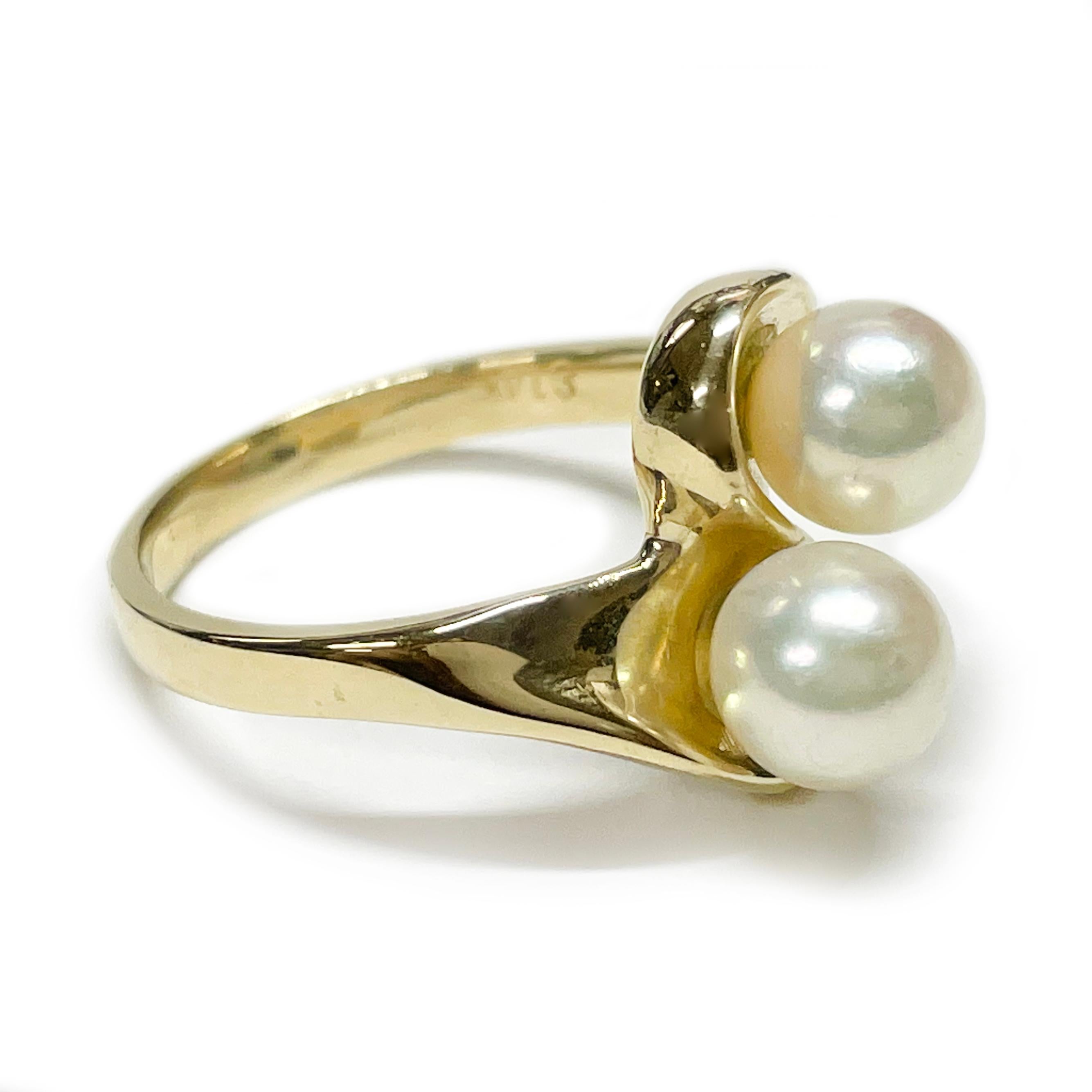 14 Karat Yellow Gold Two Pearl Ring. The ring features two swooshes for the band that meet at the center and have a pearl each. The two round 6.5mm cultured pearls are creamy white in color with good luster. Stamped on the inside of the band is E
