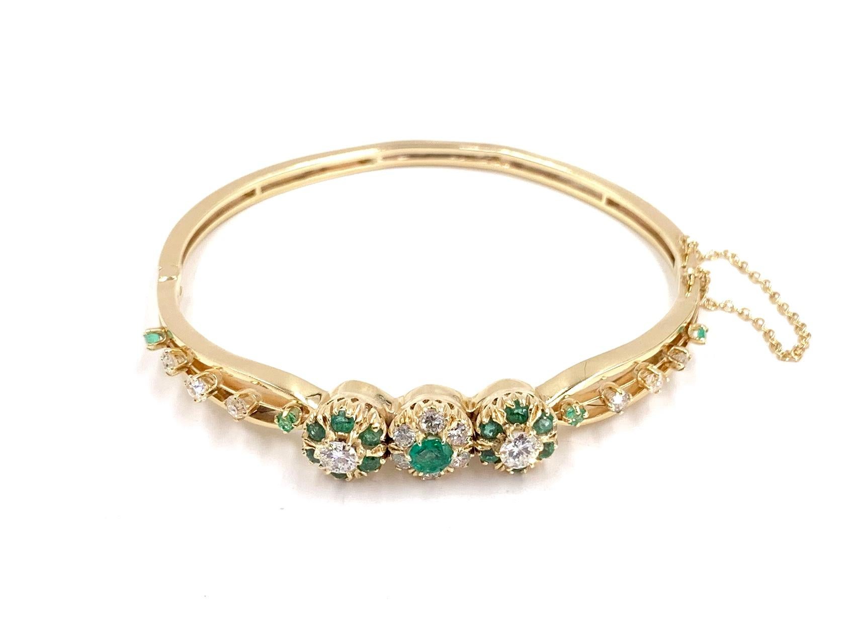An elegant 14 karat yellow gold hinged bangle bracelet featuring approximately .75 carats of white diamonds and .70 vibrant emeralds. Diamonds and emeralds are arranged in a beautiful floral motif in center. Bracelet crafted circa 1960 however the