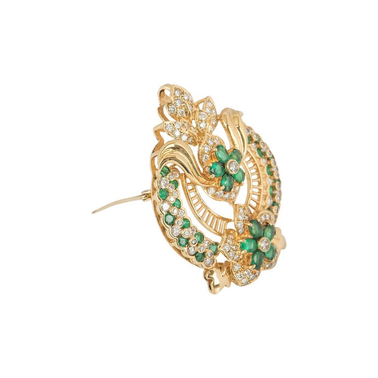 A unique 8k yellow gold diamond and emerald pendant/brooch. The brooch features an openwork floral crest set with round brilliant cut and pear cut emeralds and round brilliant cut diamonds. The emeralds have a total weight of approximately 2.83ct