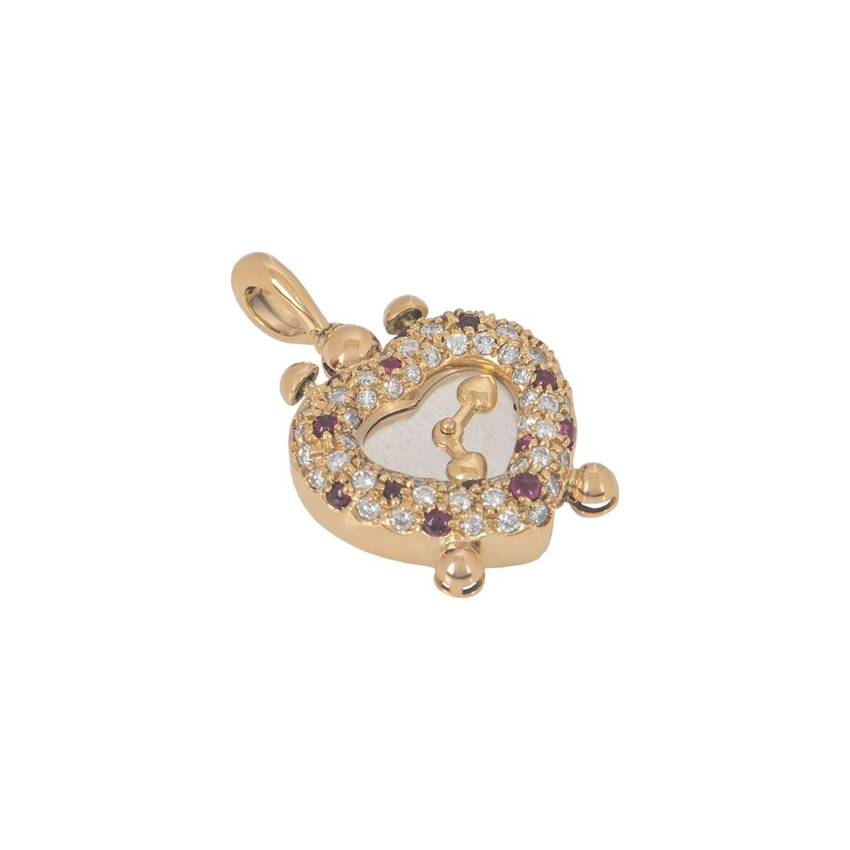 An 18k yellow gold diamond and ruby heart clock pendant. The pendant features a heart clock motif which has round brilliant cut diamonds and rubies in a pave setting alternating around the outer edge with a silver centre with gold clock hands. The