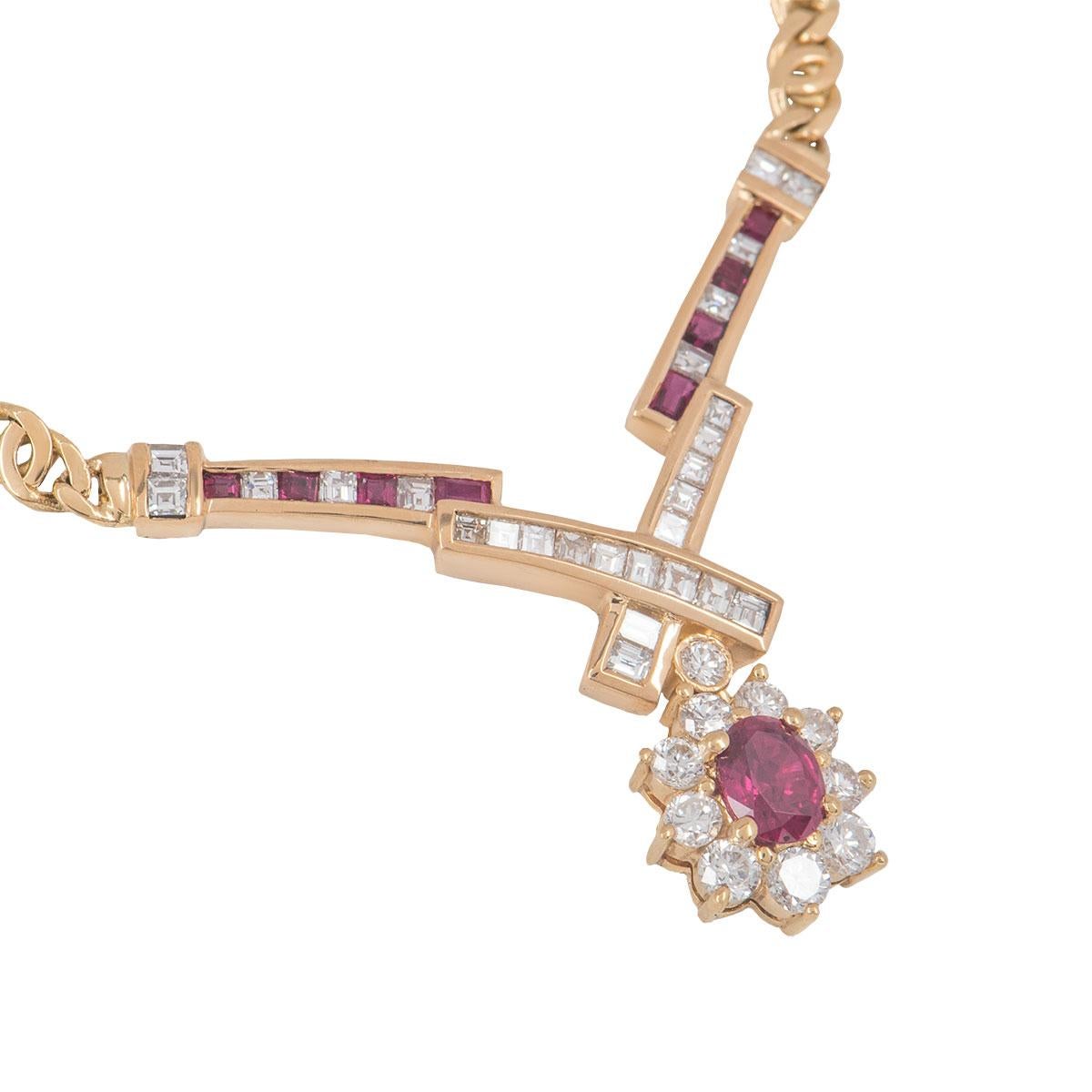 An 18k yellow gold diamond and ruby necklace. The necklace features a diamond set cross with elongated arms with alternating square emerald cut rubies and diamonds. There is a single round brilliant cut diamond in a rubover setting suspending a