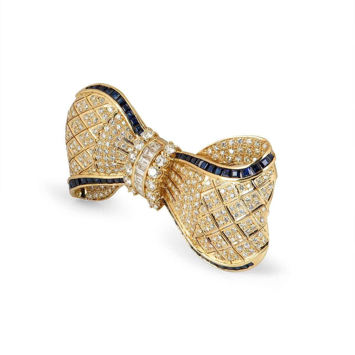 An 18k yellow gold Bow brooch. The brooch is set to the centre with baguette and round brilliant cut diamonds. The outer sides of the Bow are pave set with round brilliant cut diamonds and square cut blue sapphires. The diamonds have a total weight