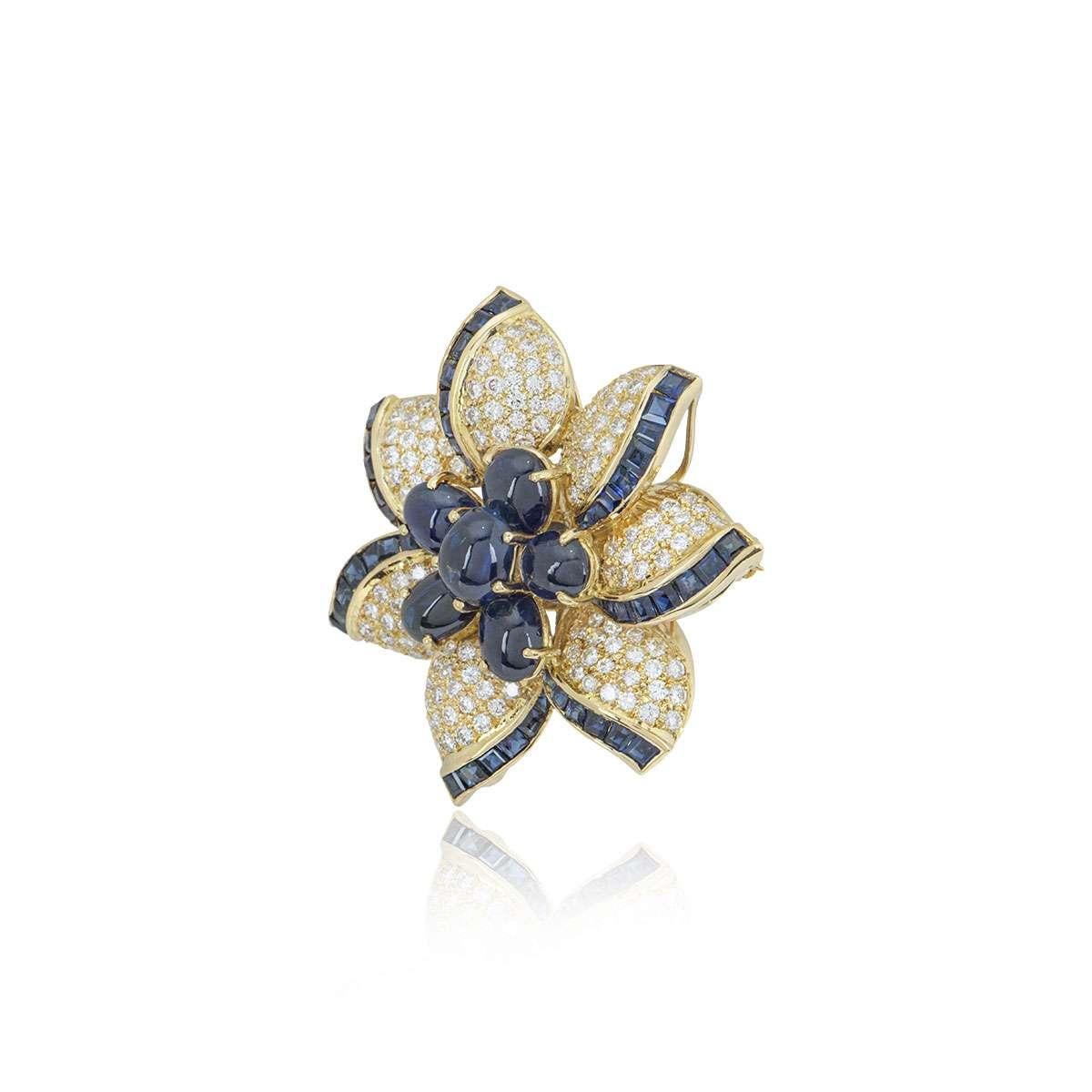 An 18k yellow gold diamond and sapphire brooch. The brooch is designed as a flower with round brilliant cut diamonds and square cut sapphires set in the petals and cabochon cut sapphires in the centre. The diamonds have a total weight of