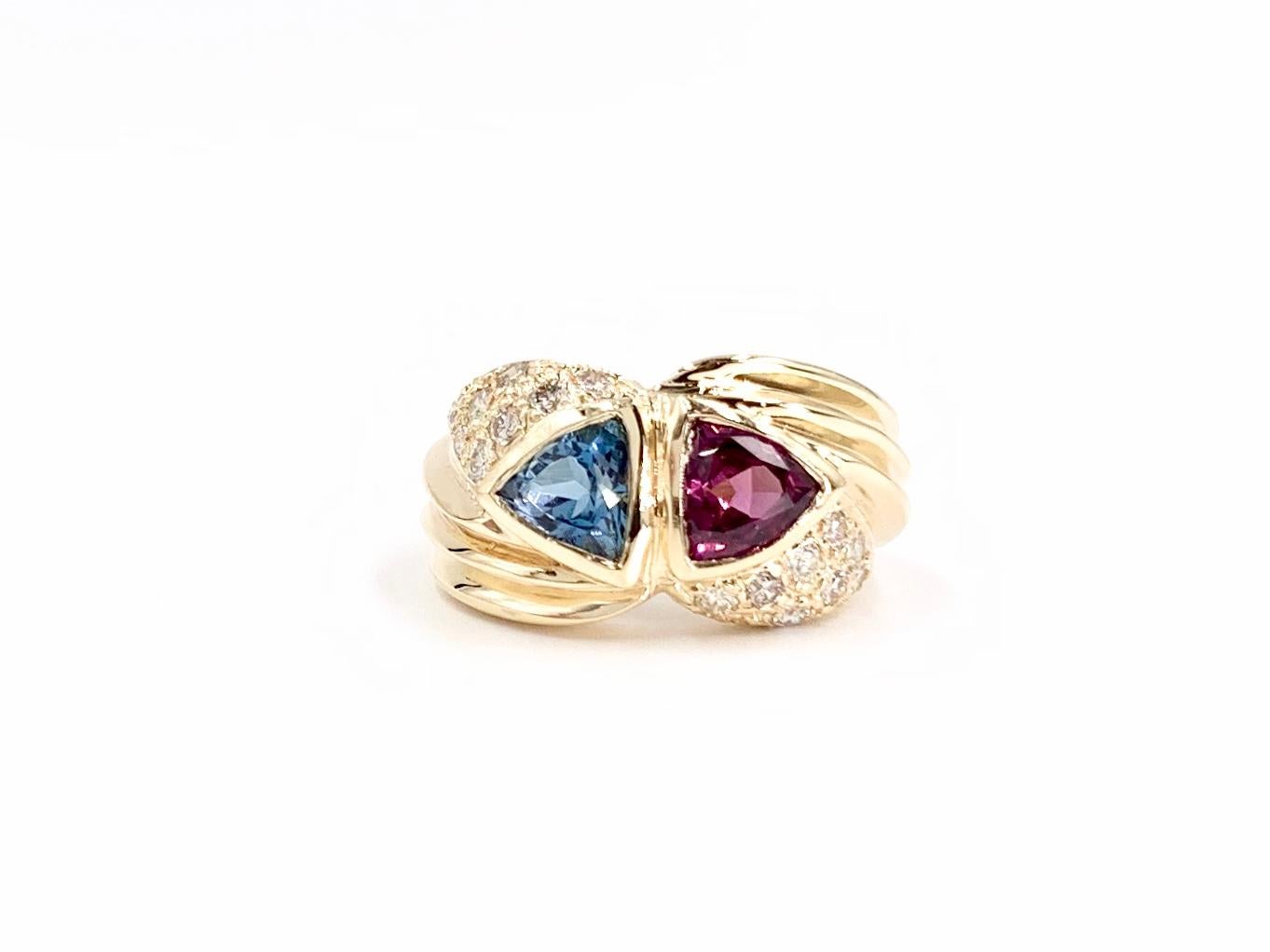A colorful, one of a kind 14 karat yellow gold modern wide ring featuring a trillion blue topaz and a trillion rhodolite garnet perfectly bezel set and accented with .48 carats of white round brilliant diamonds. Diamond quality is approximately G