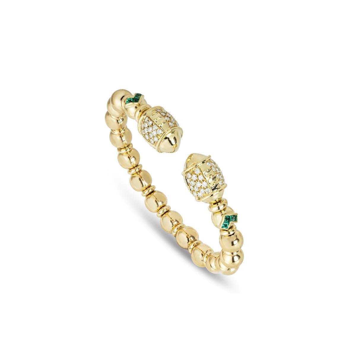 A striking 18k yellow gold diamond and emerald cuff bangle. The bracelet features two emerald stations channel set with 6 square cut emeralds with an approximate total weight of 0.30ct and displaying a vibrant green hue. Further complementing the