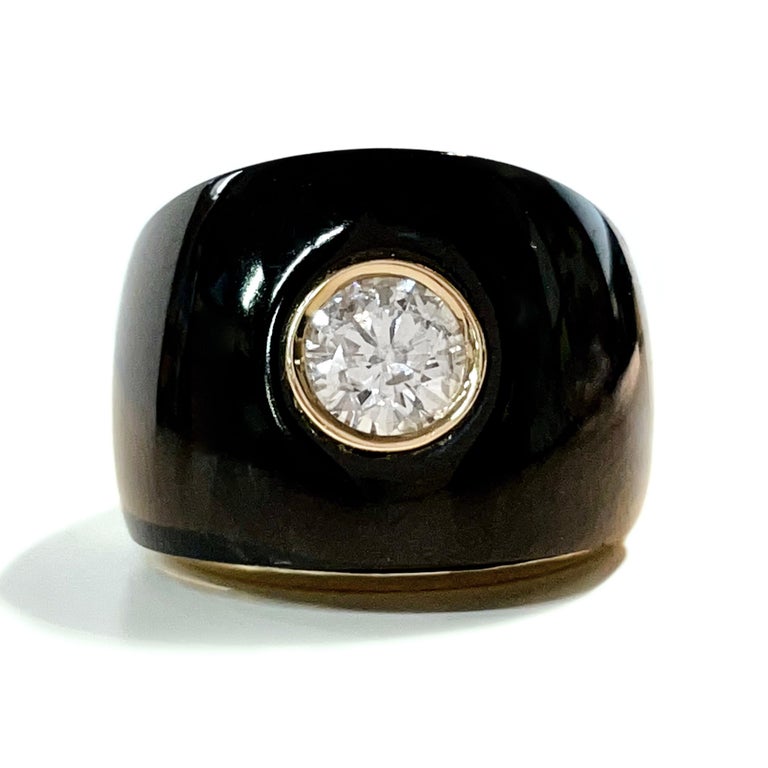 14 Karat Yellow Gold Diamond Onyx Ring. The front of the ring features a flat onyx design with a round diamond bezel-set in the center. The wide band tapers and the remainder of the ring has a smooth shiny gold finish. The center 5.2mm diamond is