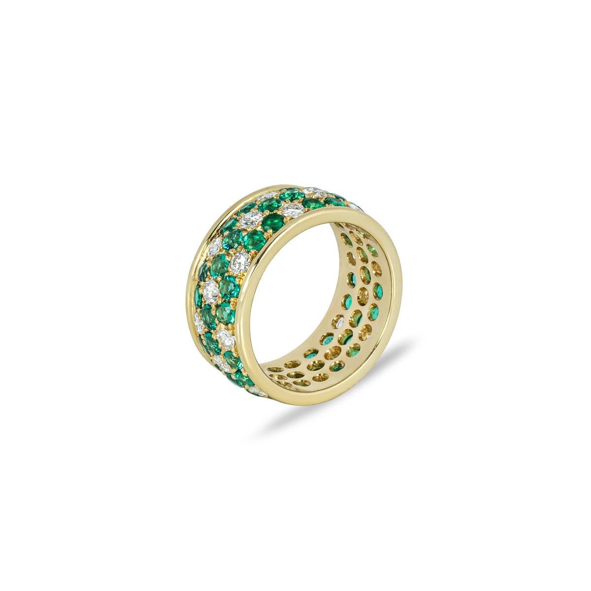 A whimsical 18k yellow gold emerald and diamond full eternity ring. The ring features 8 flower motifs each set with 6 round cut emeralds with an approximate total weight of 1.92ct and displaying a vibrant green hue. There are 24 round brilliant cut