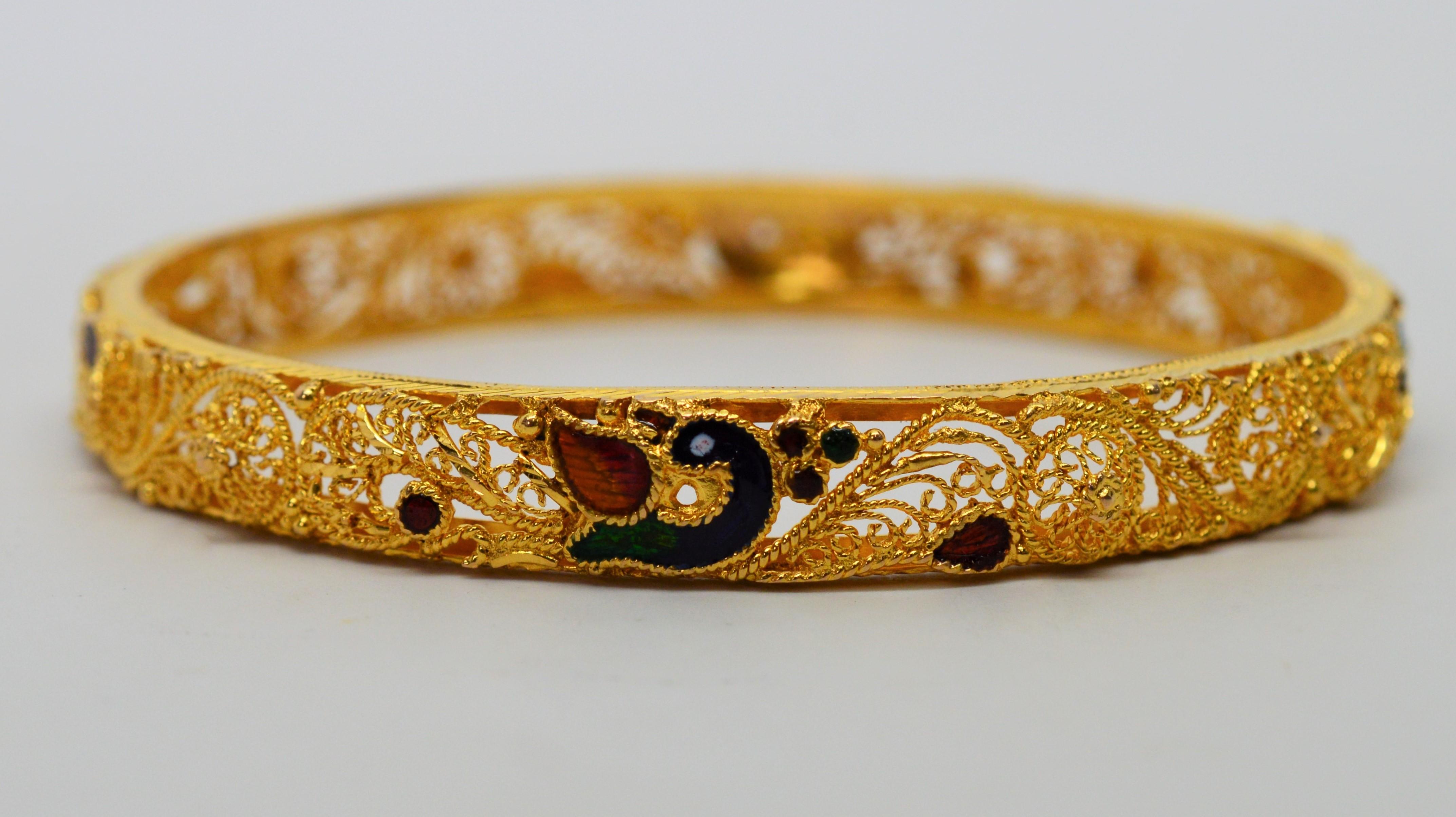Artful and elegant with an intricate filigree design made of eighteen karat 18K yellow gold, this ornate bangle bracelet is further enhanced with bright eighteen karat gold plating and colorful enamel accents. Bright hand applied enamel in rich