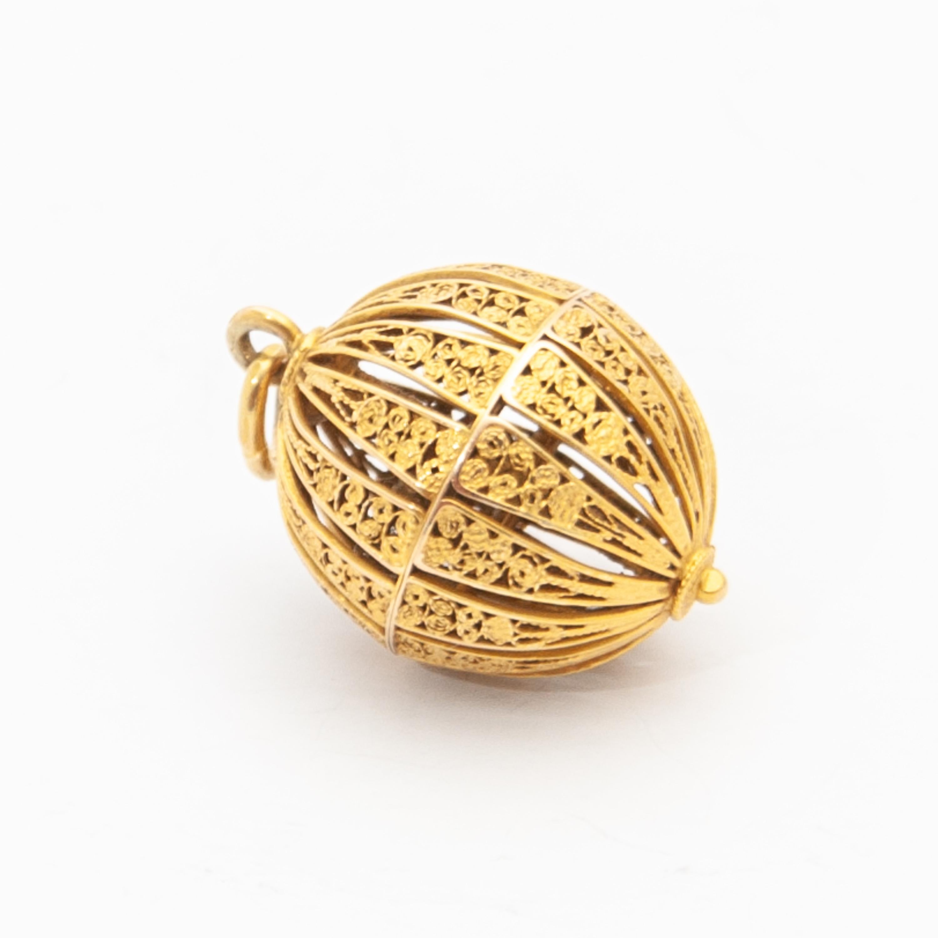 This filigree pomander pendant is crafted in 14 karat yellow gold. The lovely vinaigrette pomander is round-shaped and has an openwork design of fine filigree work. This filigree globule has a screw fitting - by unscrewing the top and bottom can be