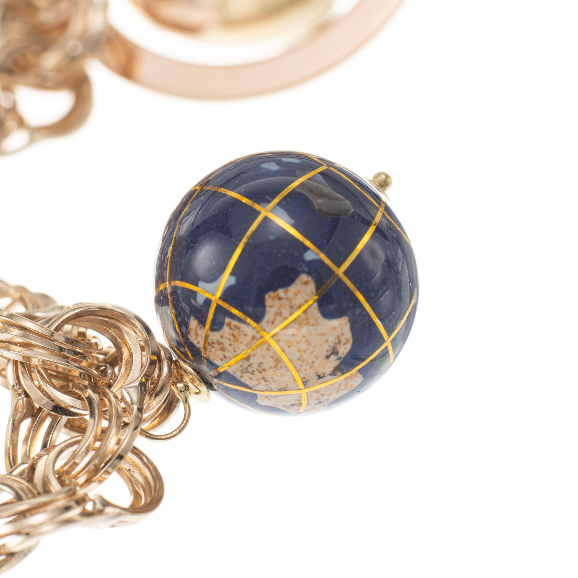 Circa 1940's five spinning globe three dimensional charm bracelet. Triple spiral link charm bracelet. Two of the charms are blue with stone inlay, two are all gold, one has cultured pearls inside and one has 5 accent cabochon emeralds. The base of