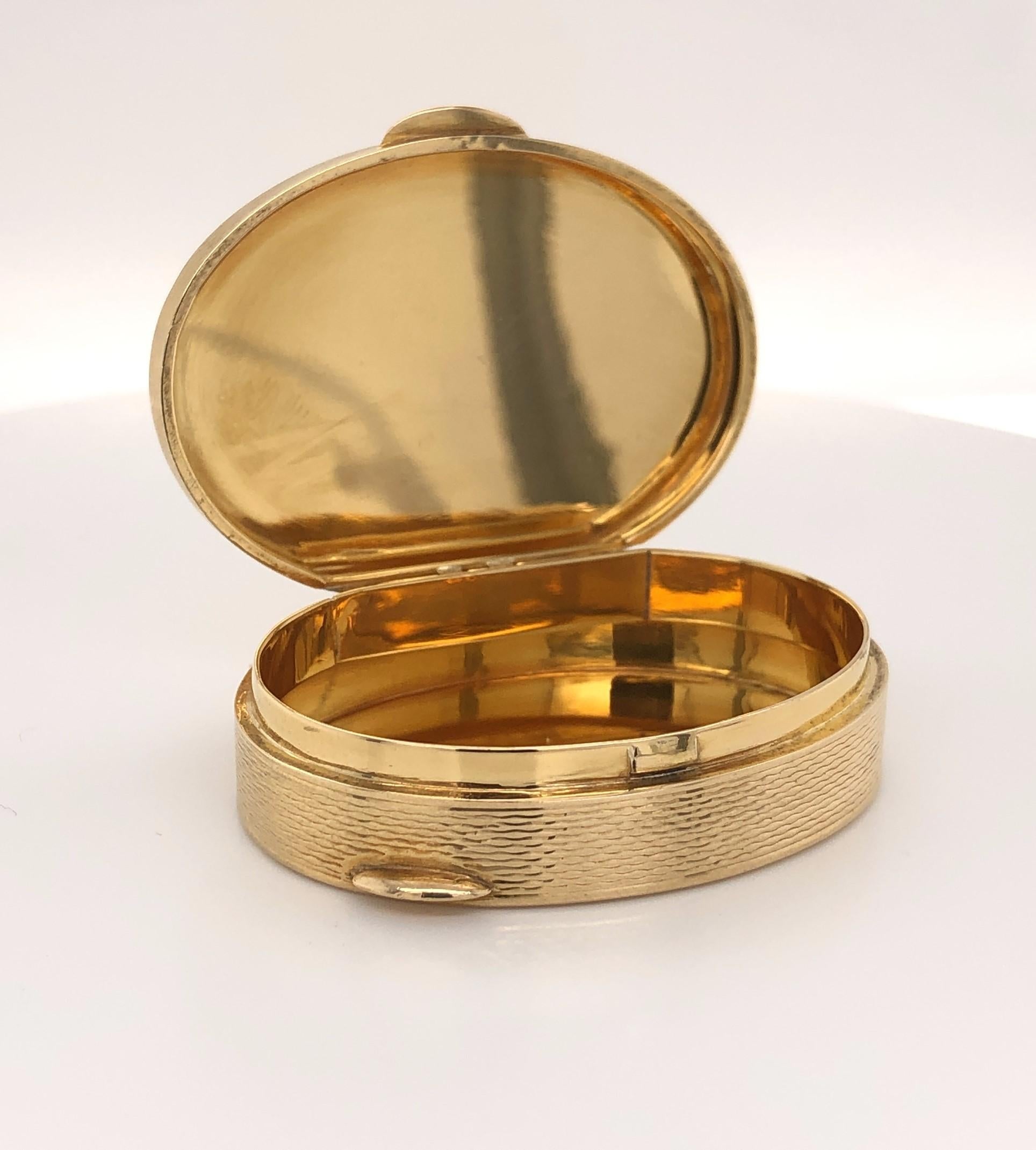 Finely finished in eighteen karat 18K yellow gold, this luxury oval pill box is a fine adornment for any vanity. Measuring 1-5/8 inch wide by  l-1/2 inch long and 3/8 inch deep, the textured gold personal pill box is fitted with two tabs and a