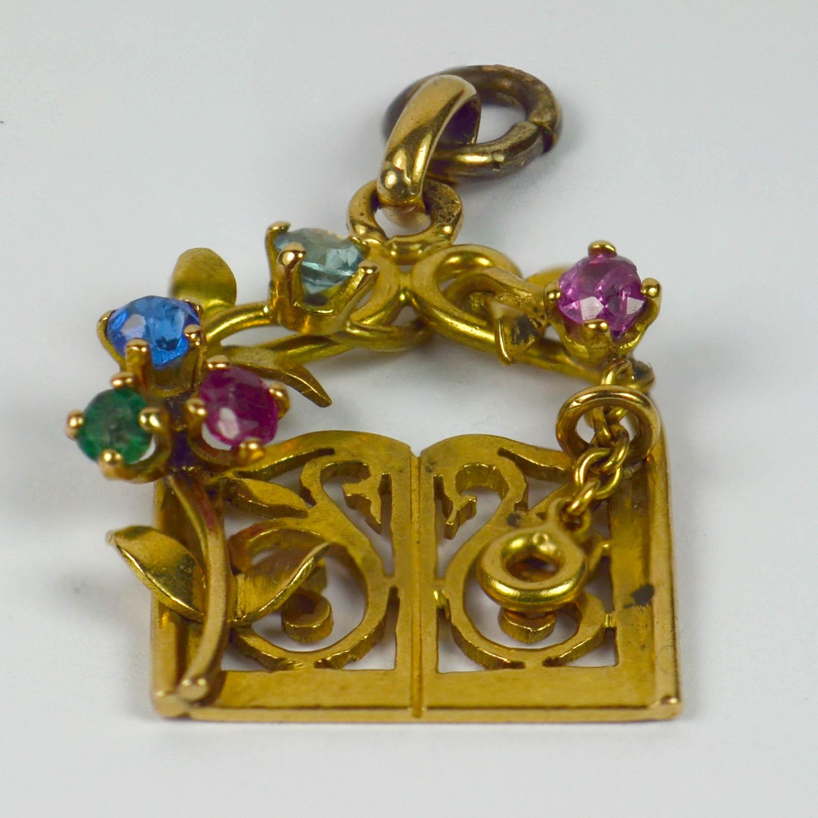 An 18 karat yellow gold charm pendant designed as a pair of garden gates with curlicue swan motif, surrounded by a gem set flowering vine. The flowers are depicted in round cut pink, red, blue and green paste. Stamped with the owl mark for French