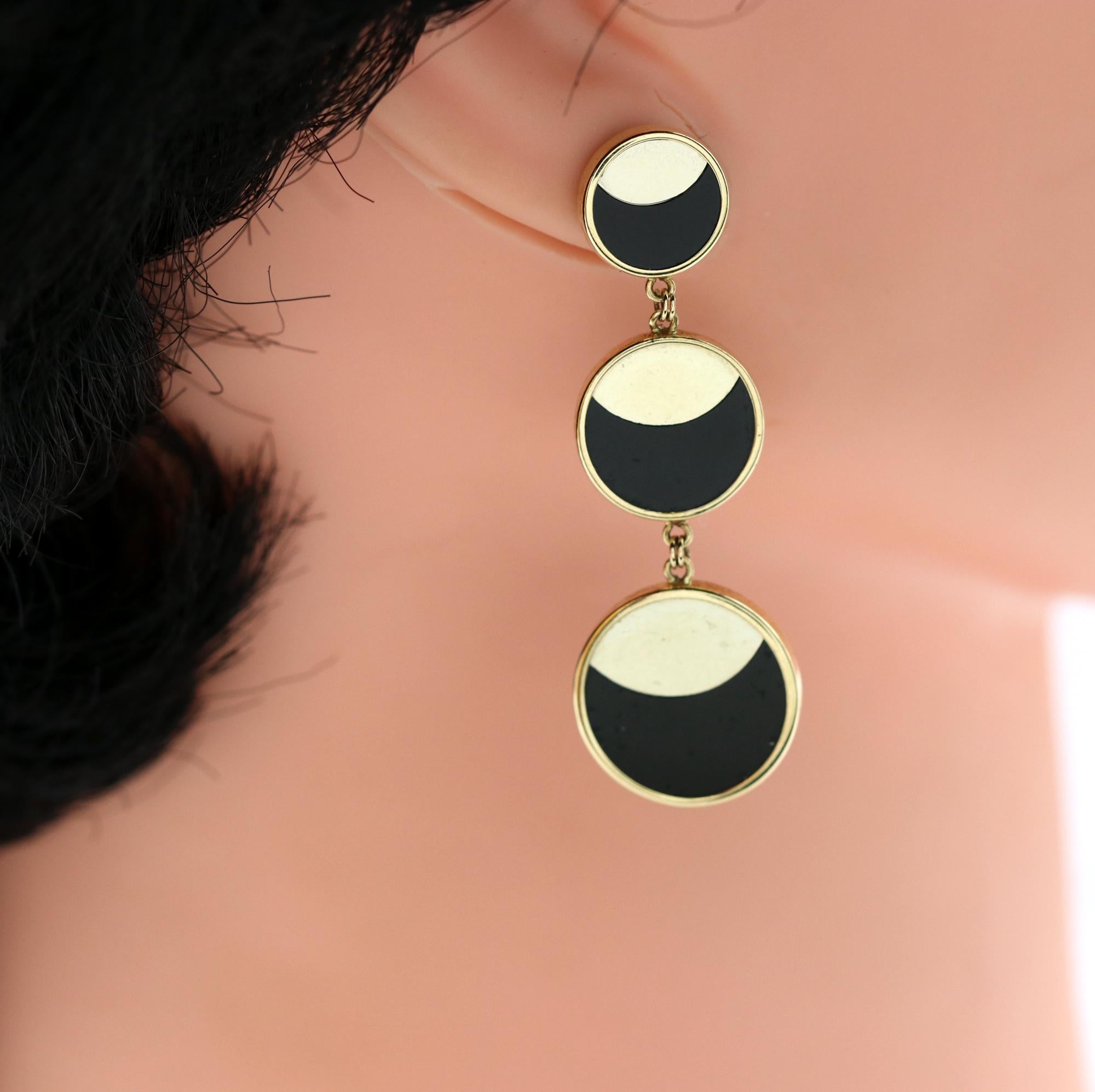 A pair of 14K yellow gold earrings with three discs graduating in size from 3/8 of an inch to 5/8 of an inch, to 3/4 of an inch. Each round station is set with onyx meeting beautifully with the gold to create a crescent moon design. Measuring 2