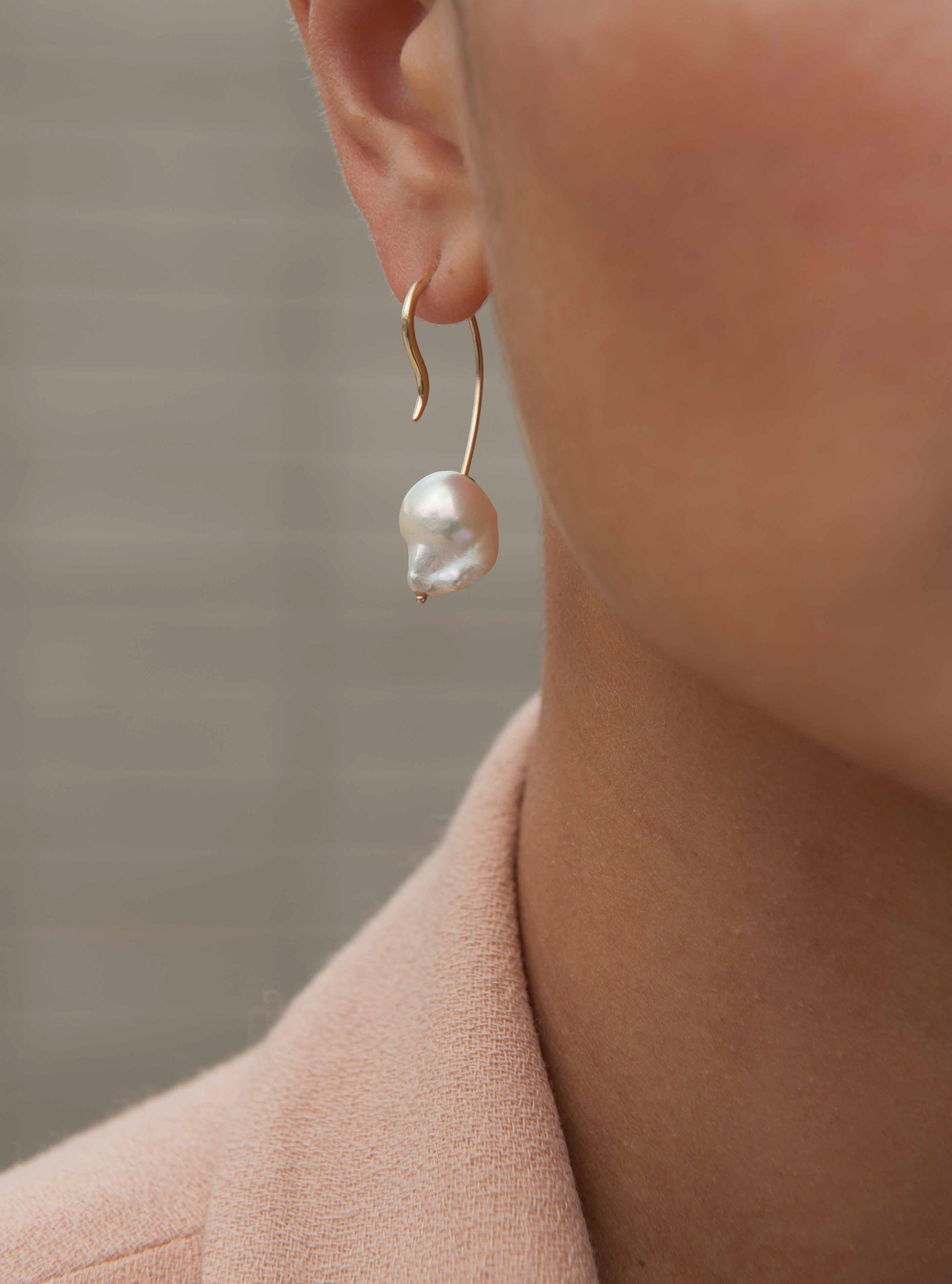 Elegantly carved by nature, a beautifully organic baroque pearl descends from behind the ear, suspended by a streamlined 14k recycled gold curve.  The delicate feminine curves of the minimalist gold earring play beautifully against the baroque