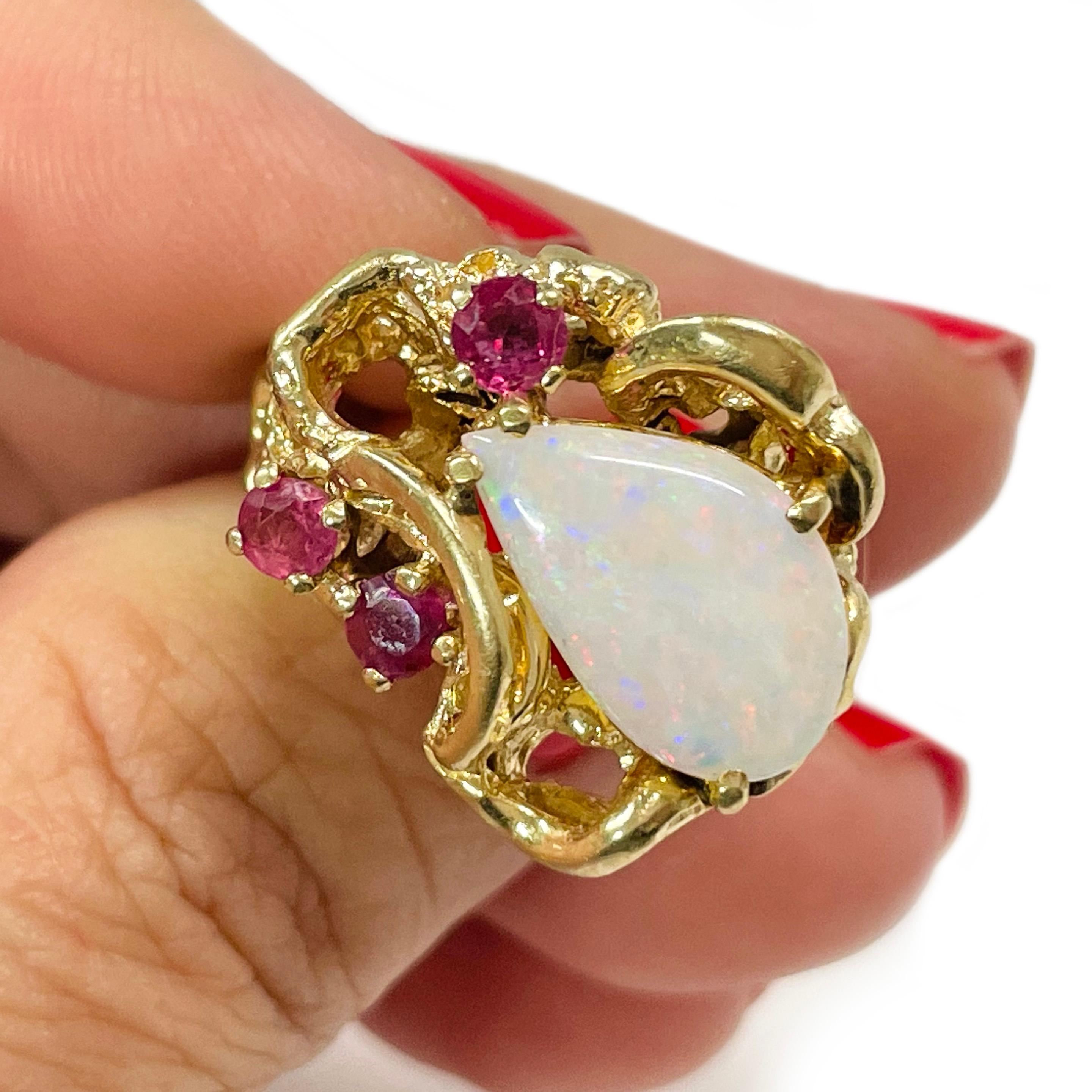 14 Karat Yellow Gold Opal Ruby Ring. The ring features a fancy opal measuring 13.2 x 8.5mm. The opal is prong-set with gold swirl and nugget asymmetrical designs. Prong-set on one side of the opal are 3 round rubies. The rubies measure 3.5mm and