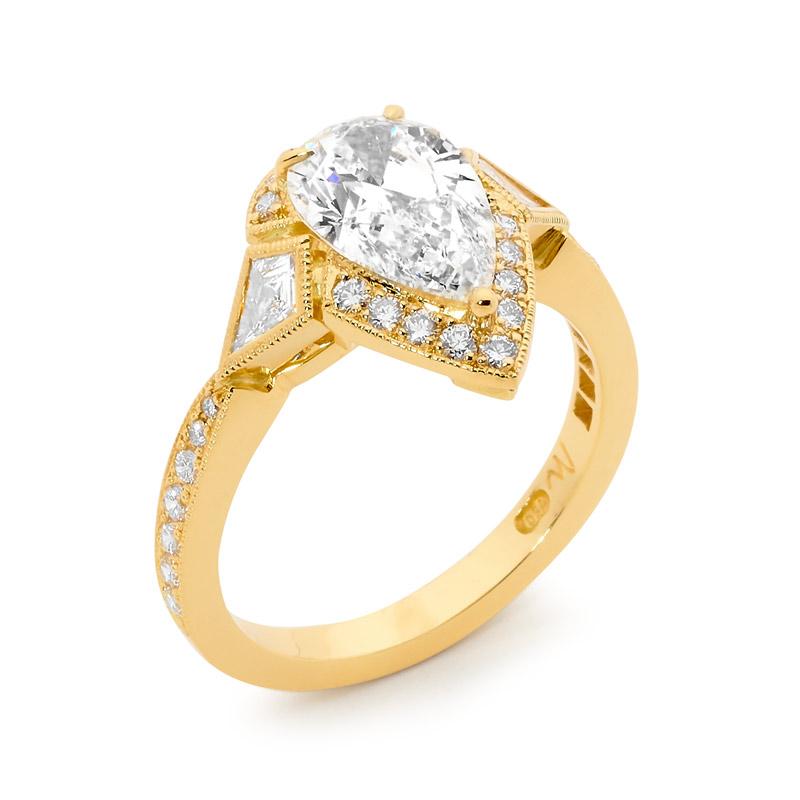 This stunning Matthew Ely engagement ring is handmade in 18ct Yellow Gold, and features a 2.01ct Pear Shaped Diamond with 2 Kite Shaped Diamonds equalling 0.21ct and a halo of Round Diamonds. It can be sized on request.